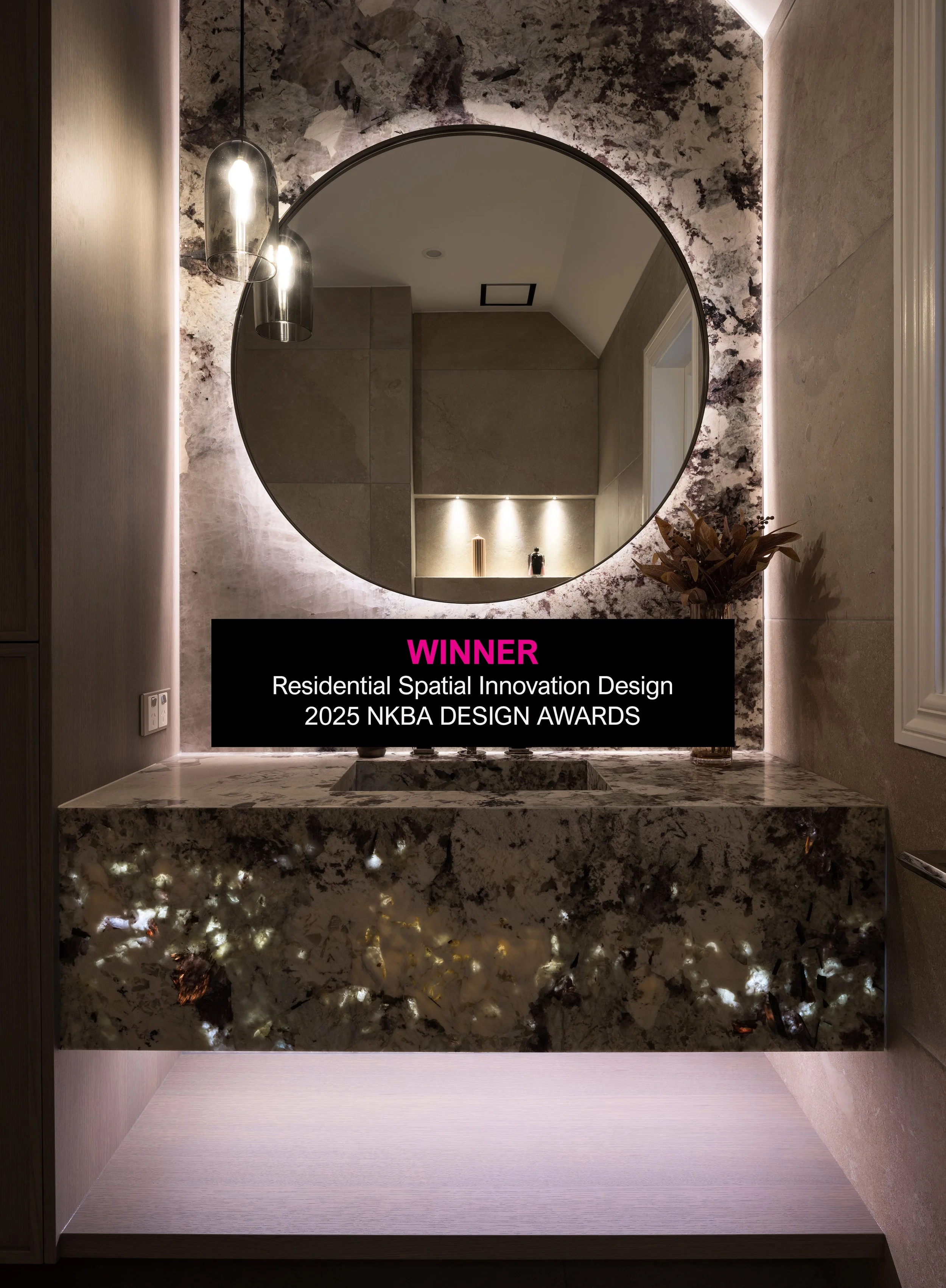 A modern bathroom with a round mirror, pendant lights, and a marble countertop. Award text overlay states 'WINNER Residential Spatial Innovation Design 2025 NKBA DESIGN AWARDS'.