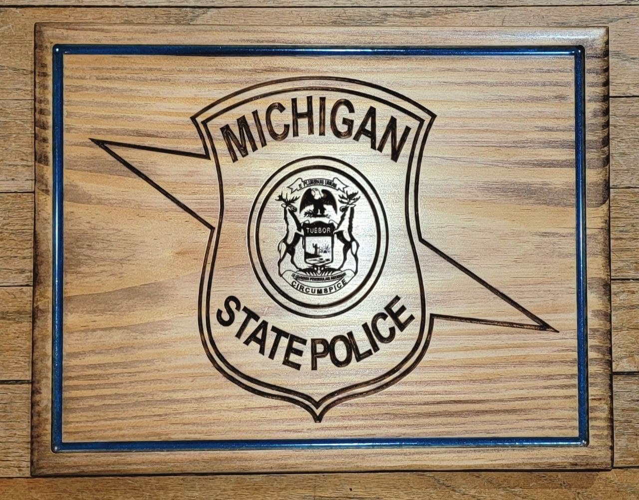 This Michigan State Police wooden plaque is made from 3/4” solid wood and measures approximately 10.5” x 13.5. The plaque pictured has an optional blue line frame.