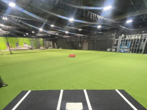 Indoor sports training facility with artificial turf and workout equipment.
