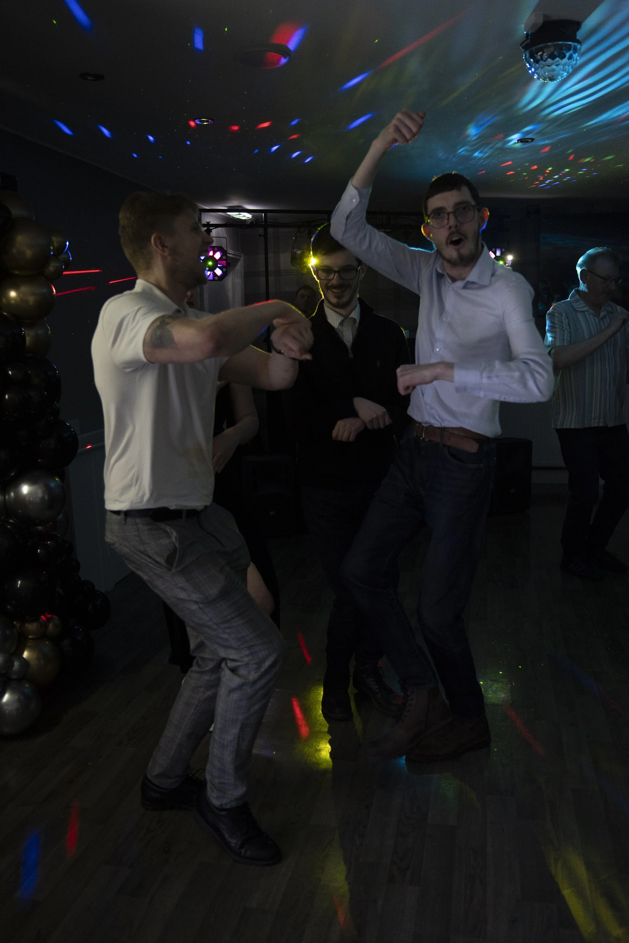 People dancing and having fun at a party under colorful lights in a dimly lit room.