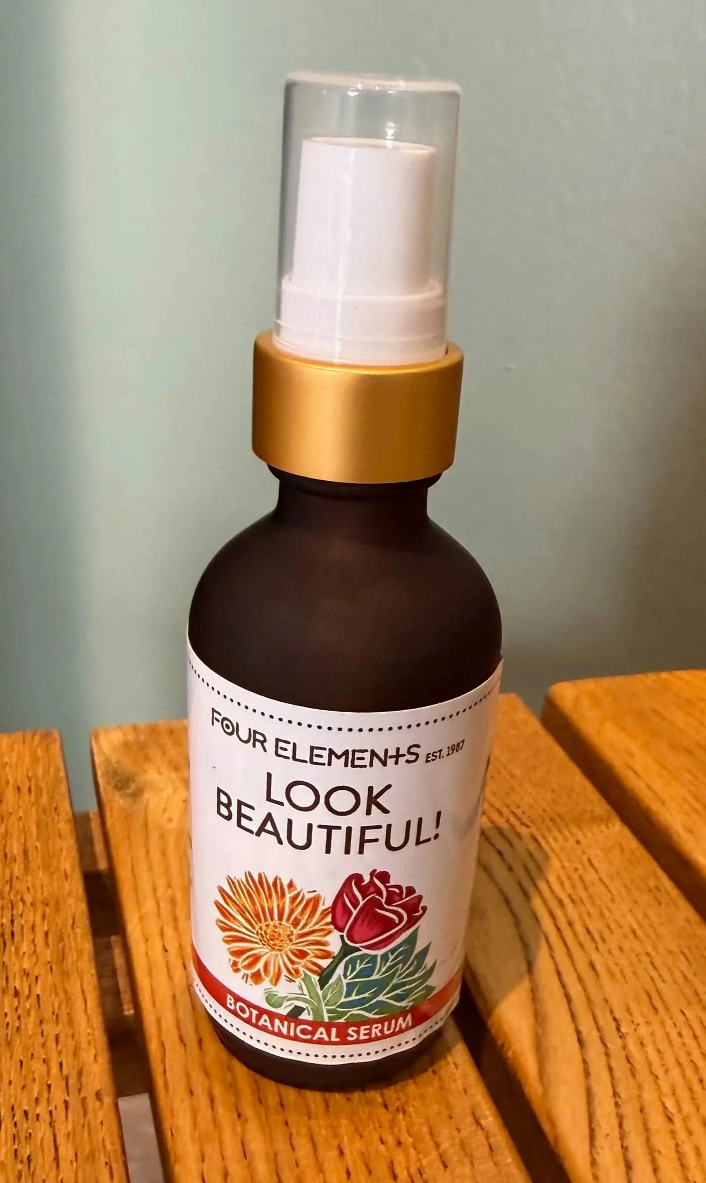 A bottle of botanical serum with a spray top, placed on a wooden surface.