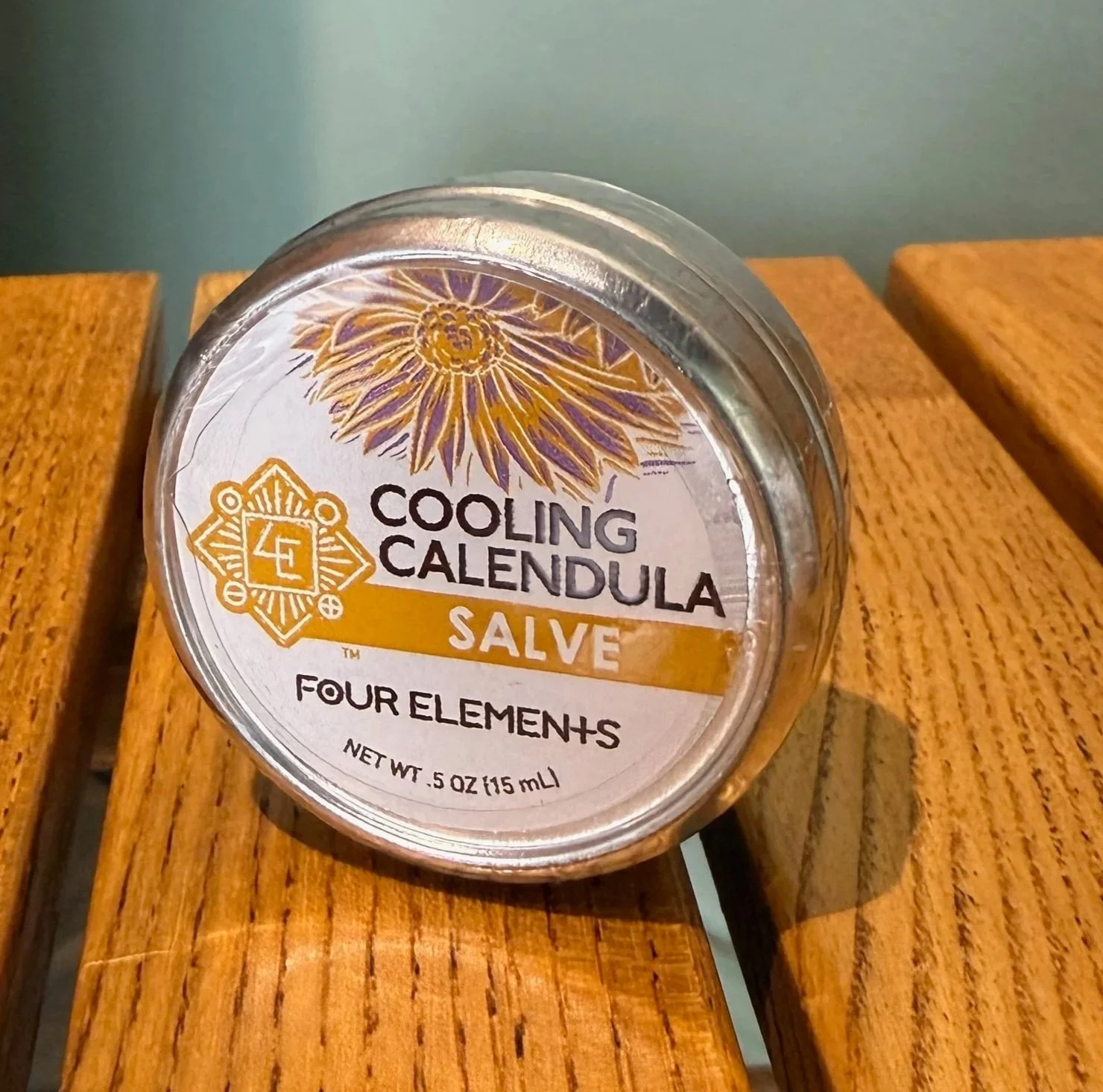 A container of Four Elements Cooling Calendula Salve resting on a wooden surface.
