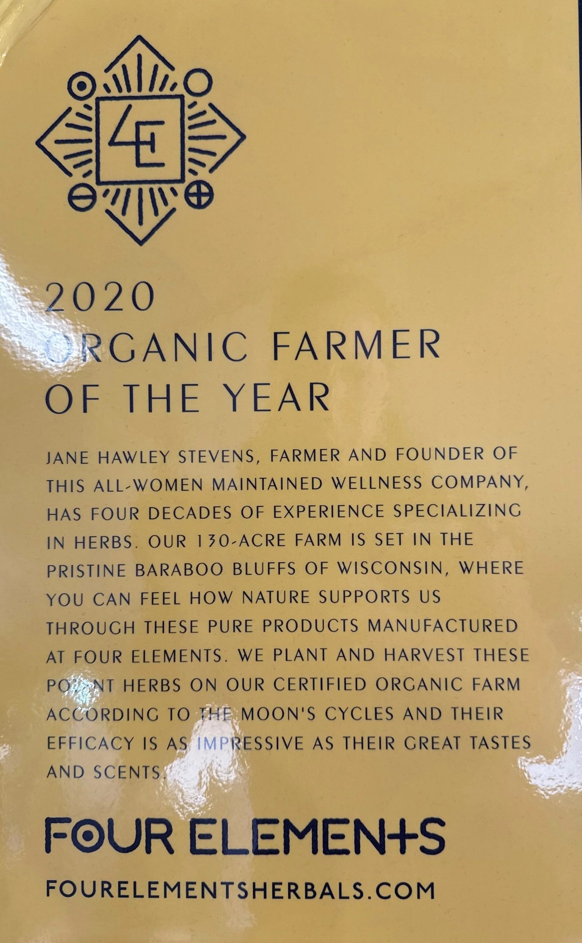 Text and logo on a yellow background with a black geometric design featuring four circles, lines, and a central symbol. The text reads: "2020 Organic Farmer of the Year" and provides information about Jane Hawley Stevens, her farm, and herbal products.