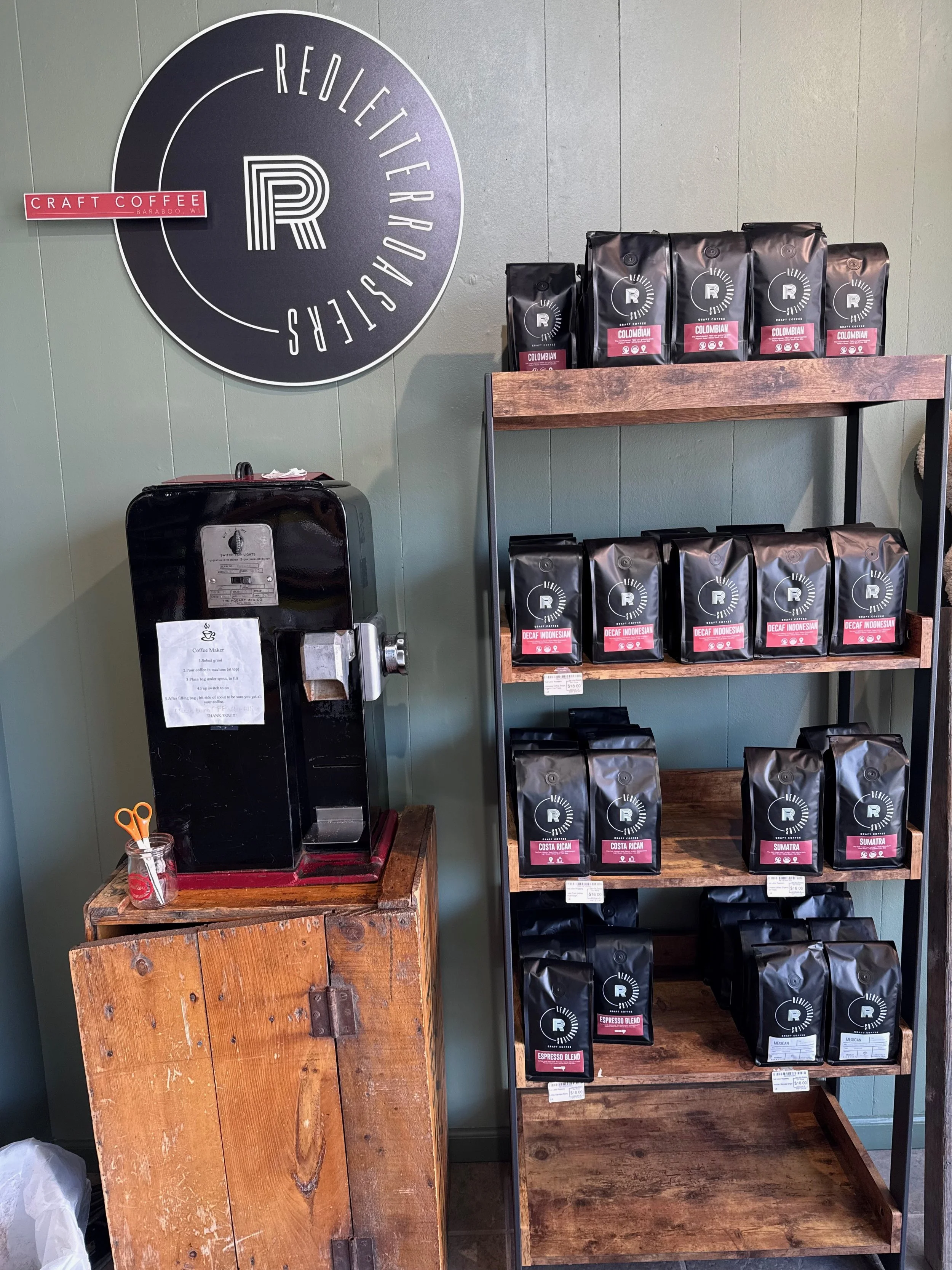 Coffee shop display with bags of coffee, a coffee machine, and a large circular sign on the wall with the words "Relietter" and an R logo, along with a red "Craft Coffee" sign.