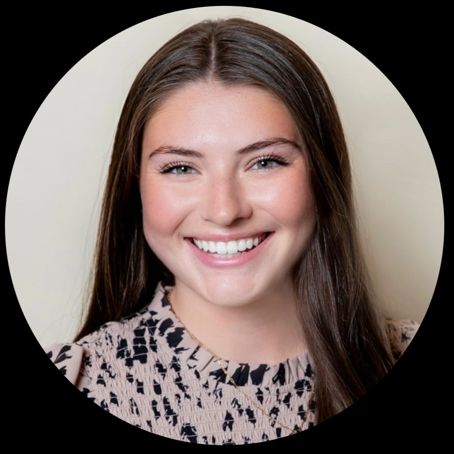 A young woman with long brown hair smiling and wearing a patterned blouse, against a light-colored background.