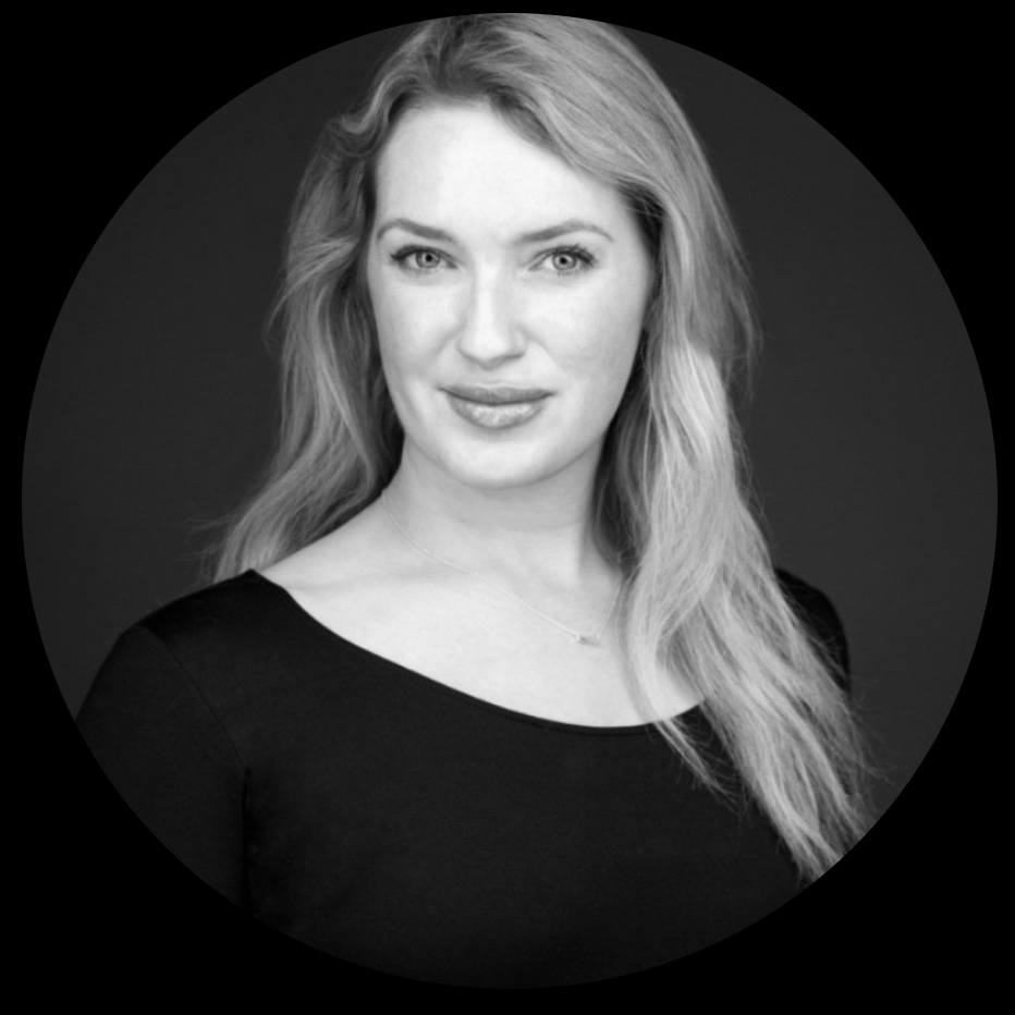 Black and white portrait of a woman with long, wavy hair wearing a black top and a delicate necklace, against a dark background.