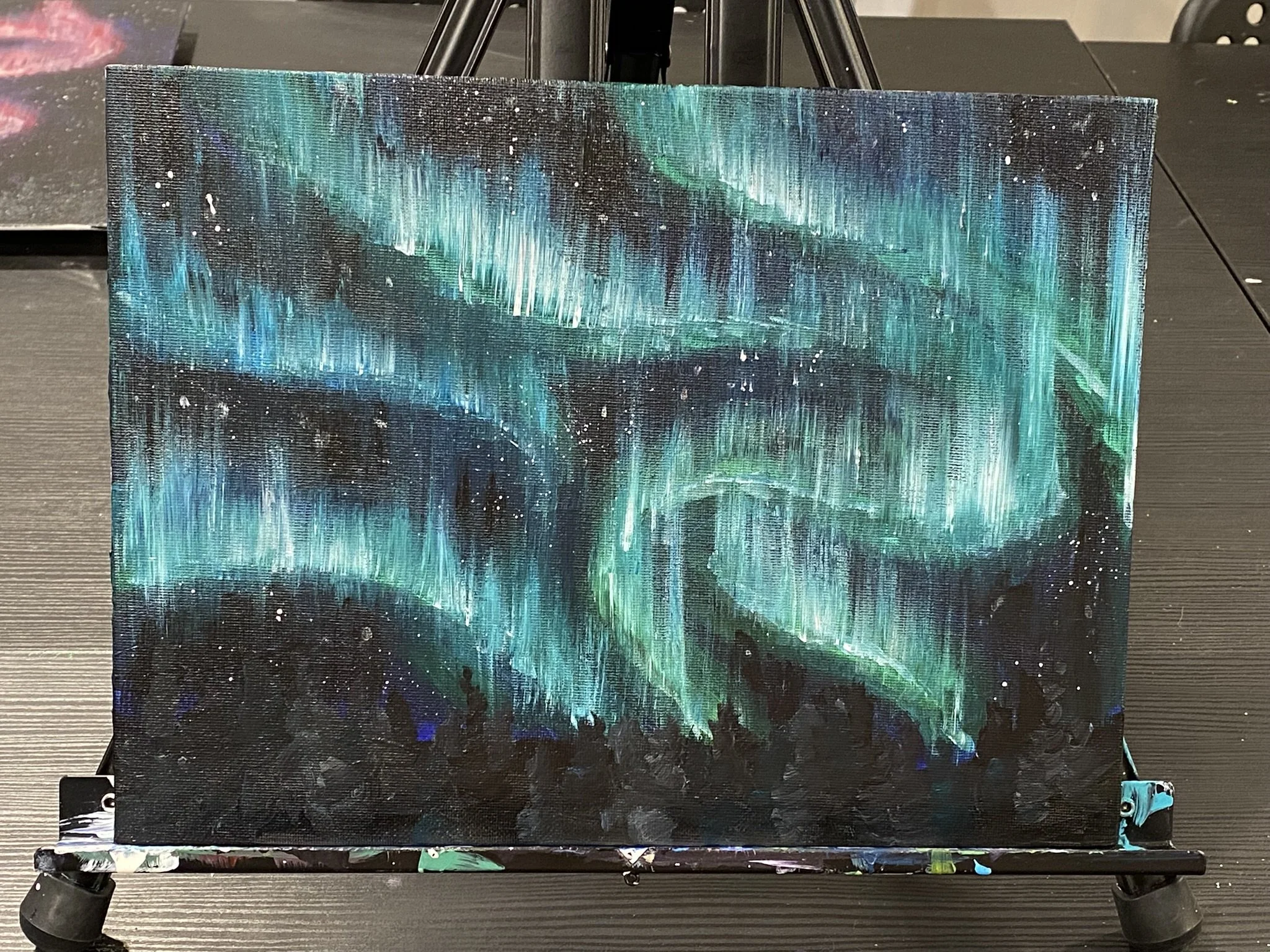 Painting of green and blue northern lights above a dark row of trees