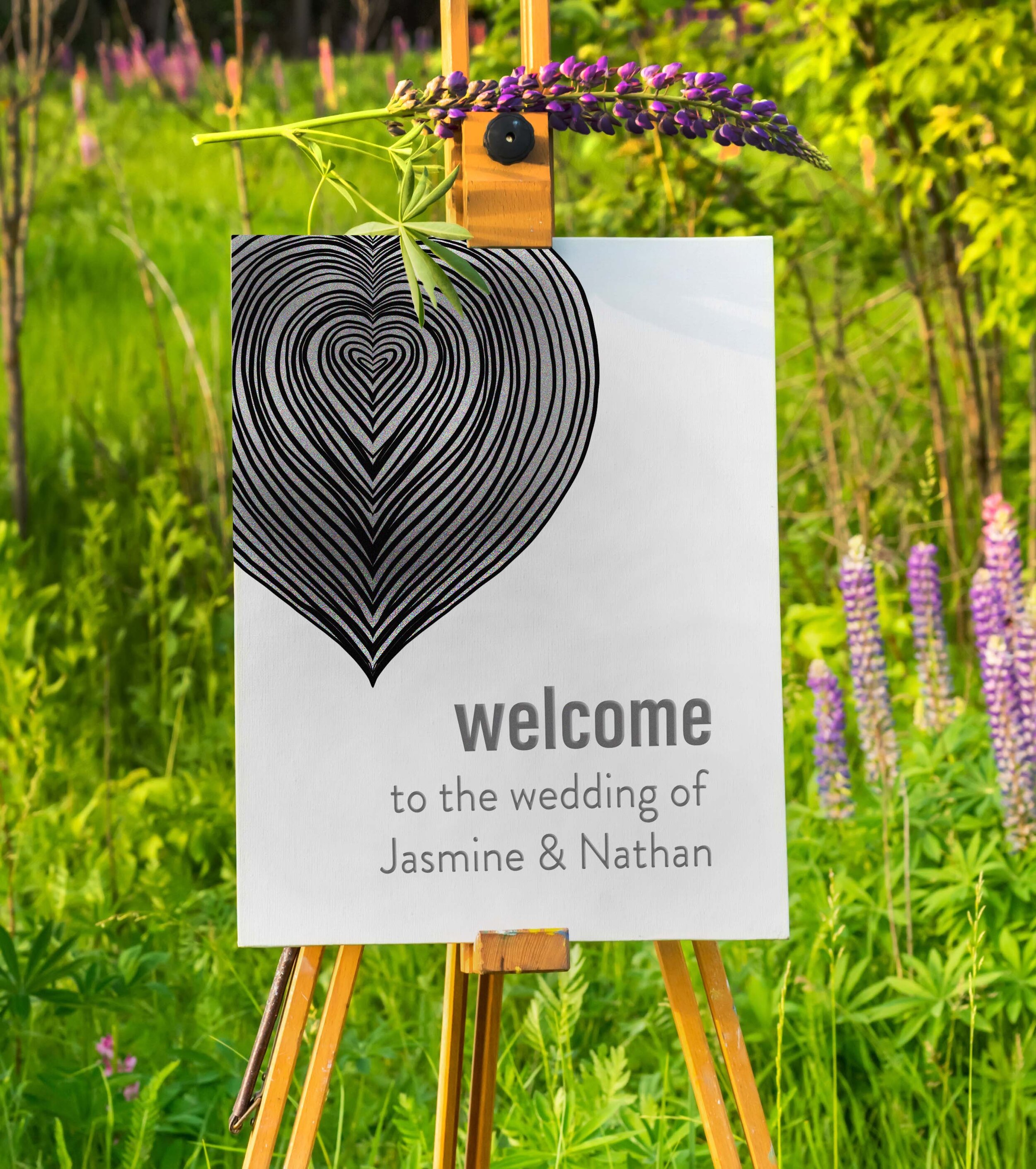 Wedding welcome sign on easel with black heart design in outdoor setting.