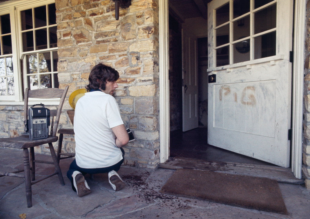 Roman Polanski klęczący obok wejścia do posiadłości przy Cielo Drive, na drzwiach słowo PIG, wymalowane przez bandę Mansona krwią swoich ofiar, fot: Julian Wasser