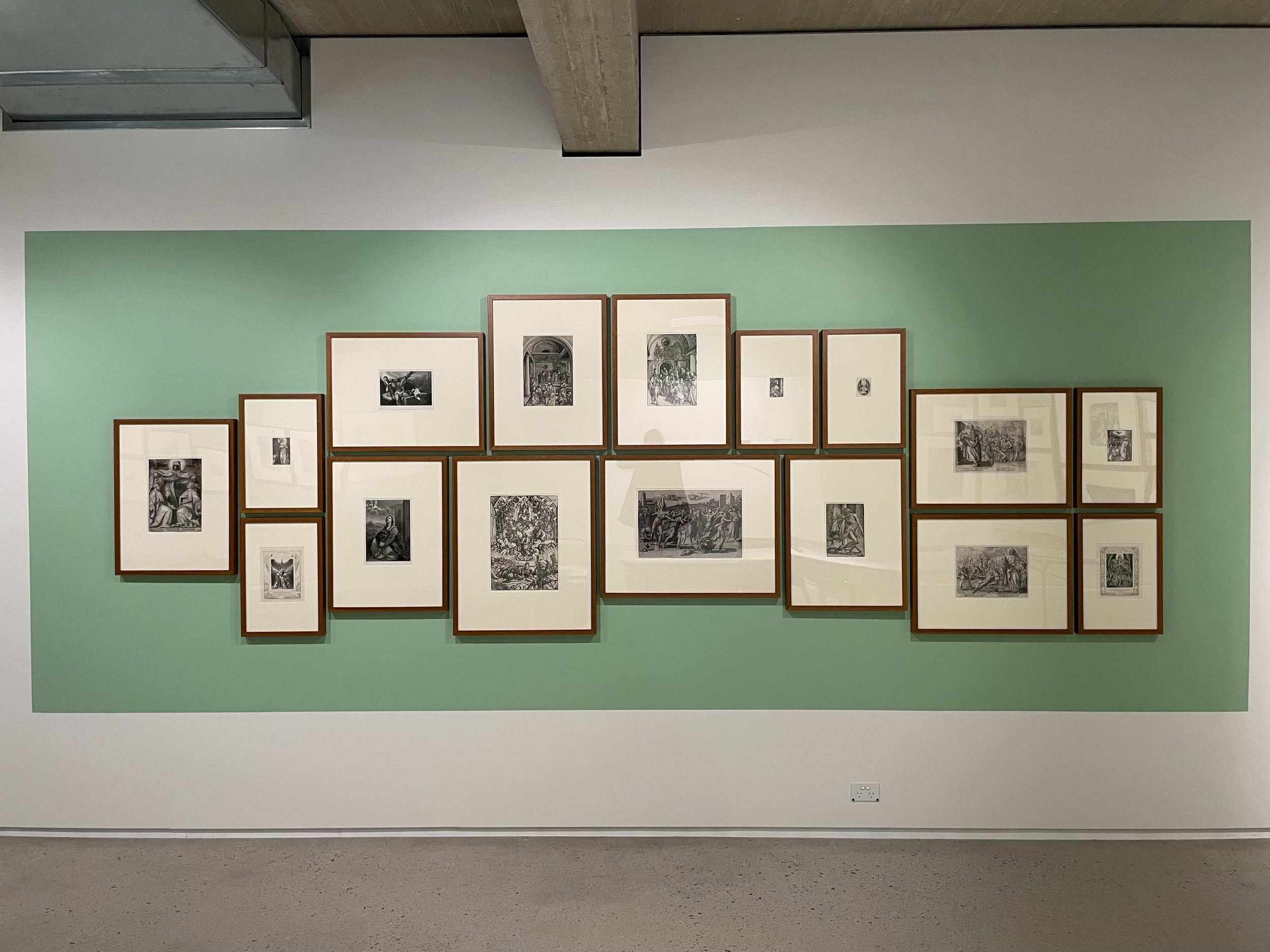 An art display with multiple framed black and white images on a light green wall in a gallery.