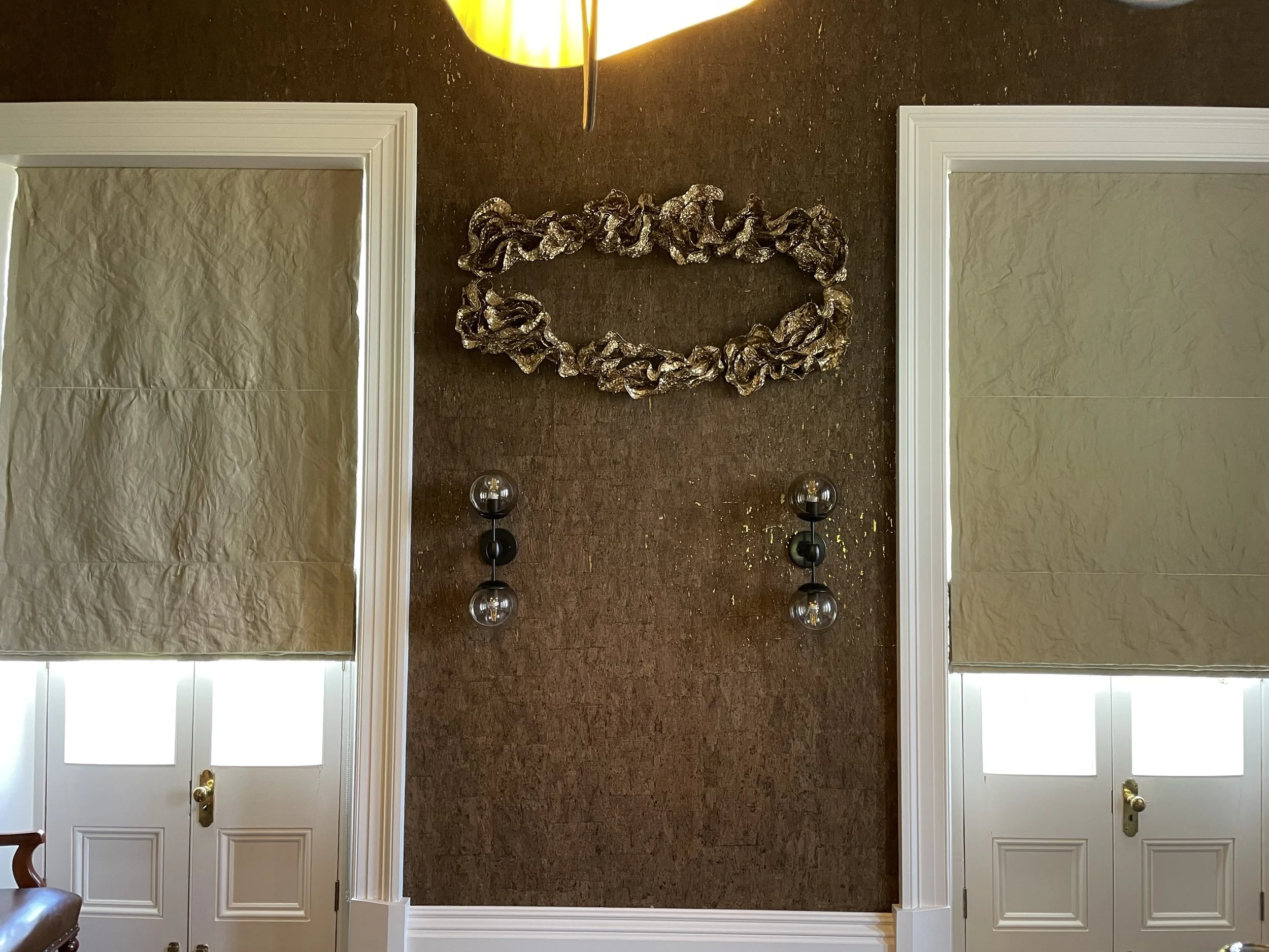 Interior wall with decorative art piece, two wall-mounted light fixtures with glass globes, and two closed doors with window panels and gold handles.