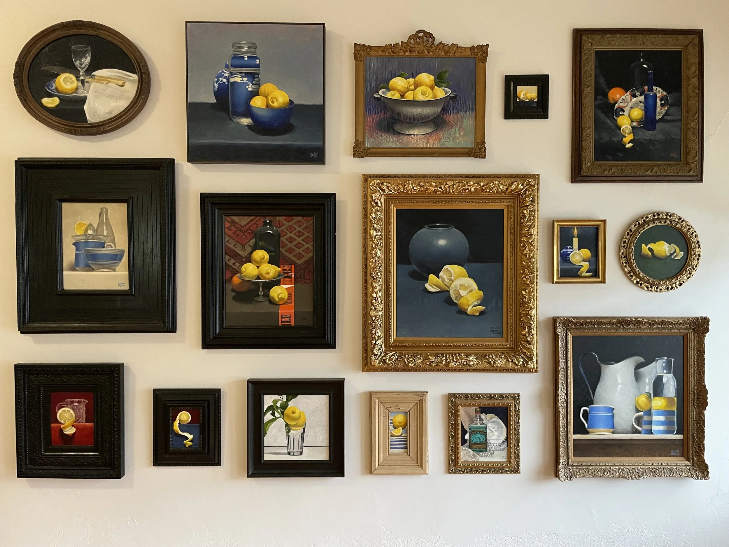 A collection of framed still life paintings featuring lemons, bottles, pitchers, and bowls, arranged on a white wall. gallery hang, art installation, art hanging, curated hanging. curation
