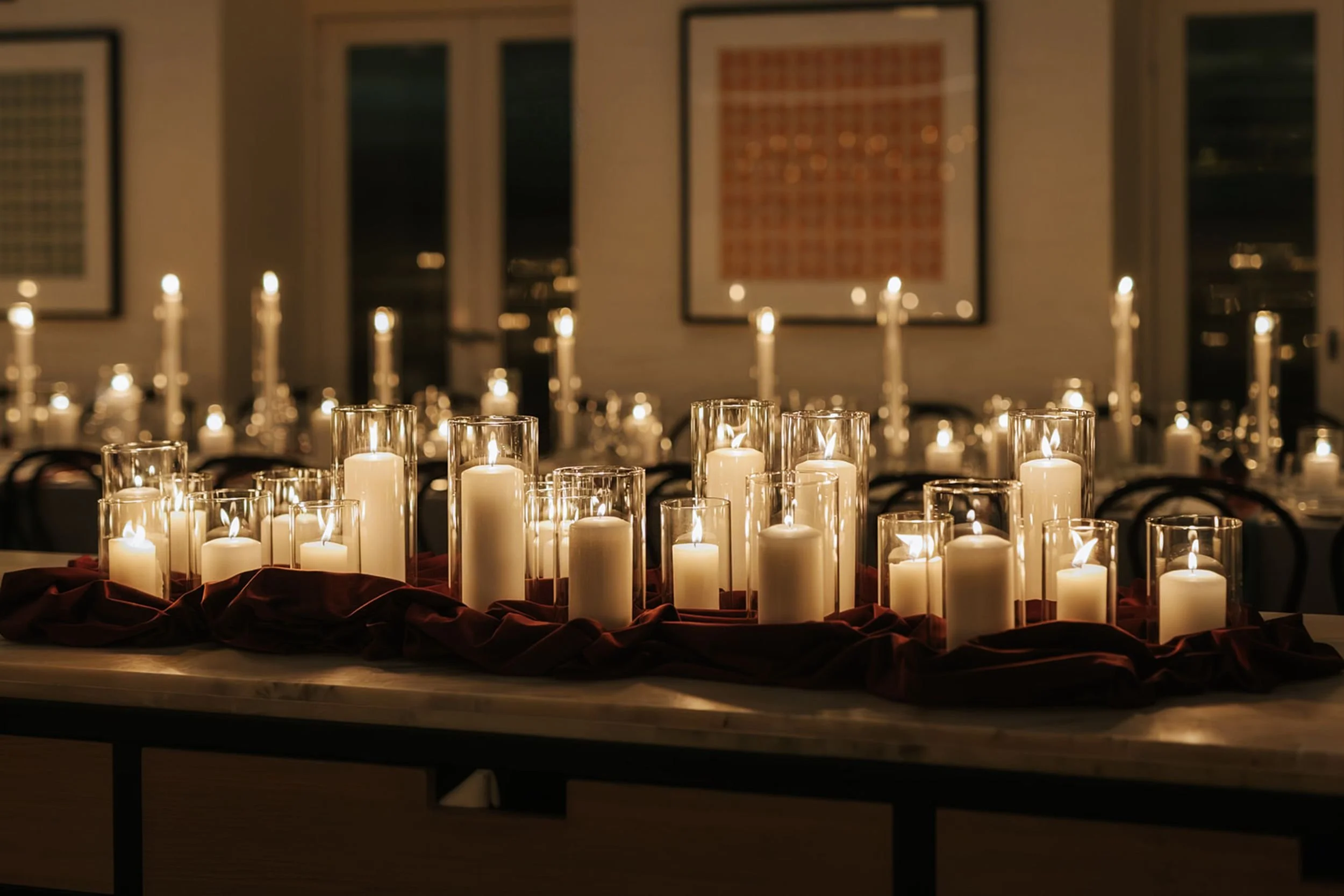 Photo by Sunny Bishop Photography.  Table decorated with numerous lit white candles in glass holders, with artwork on the wall in the background.