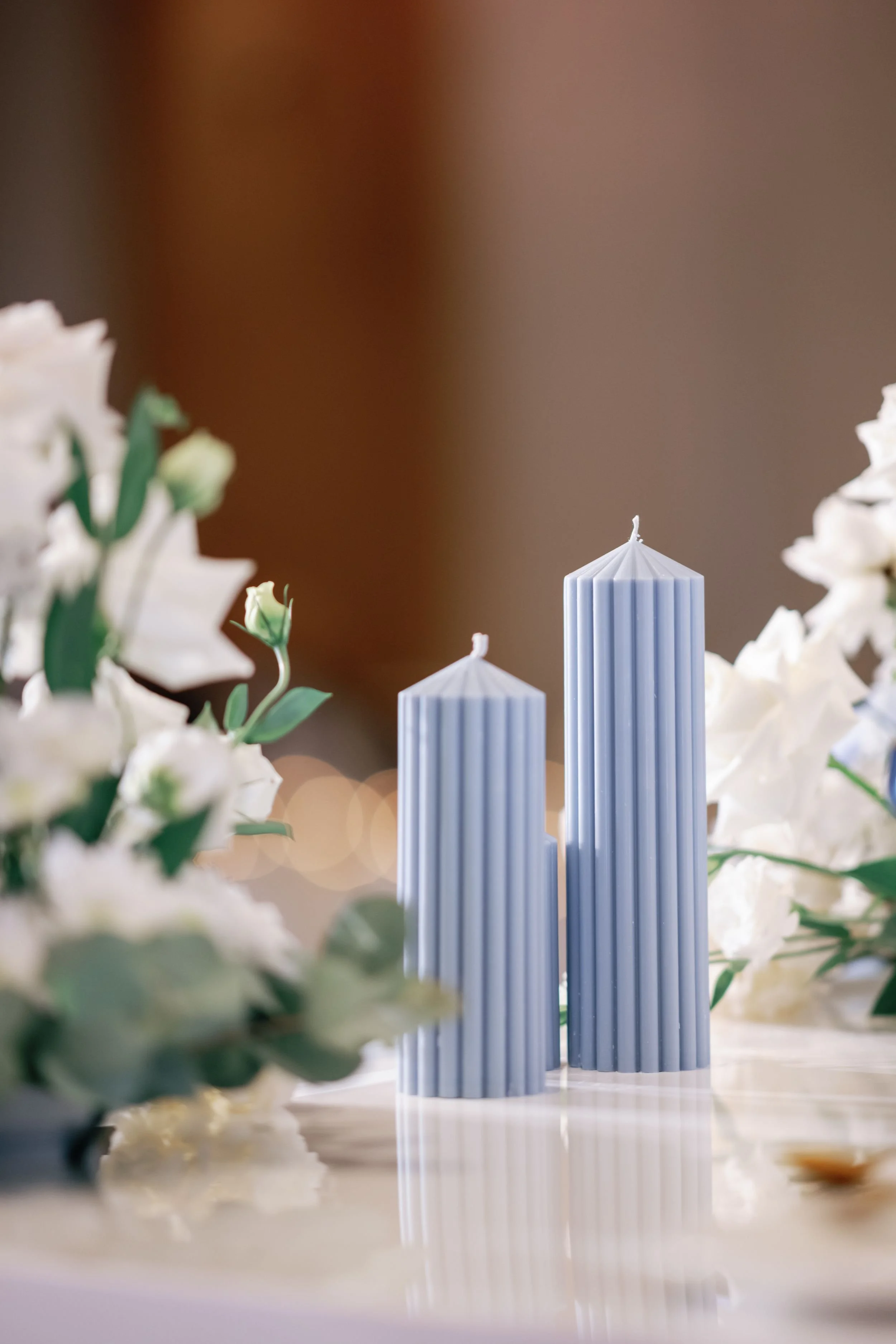 Photo by Norman Yapp Photography.  Close-up of white candles and white flowers on a table, with a blurred background.  Candle styling by Candlescapes, Perth Candle Styling & Hire.