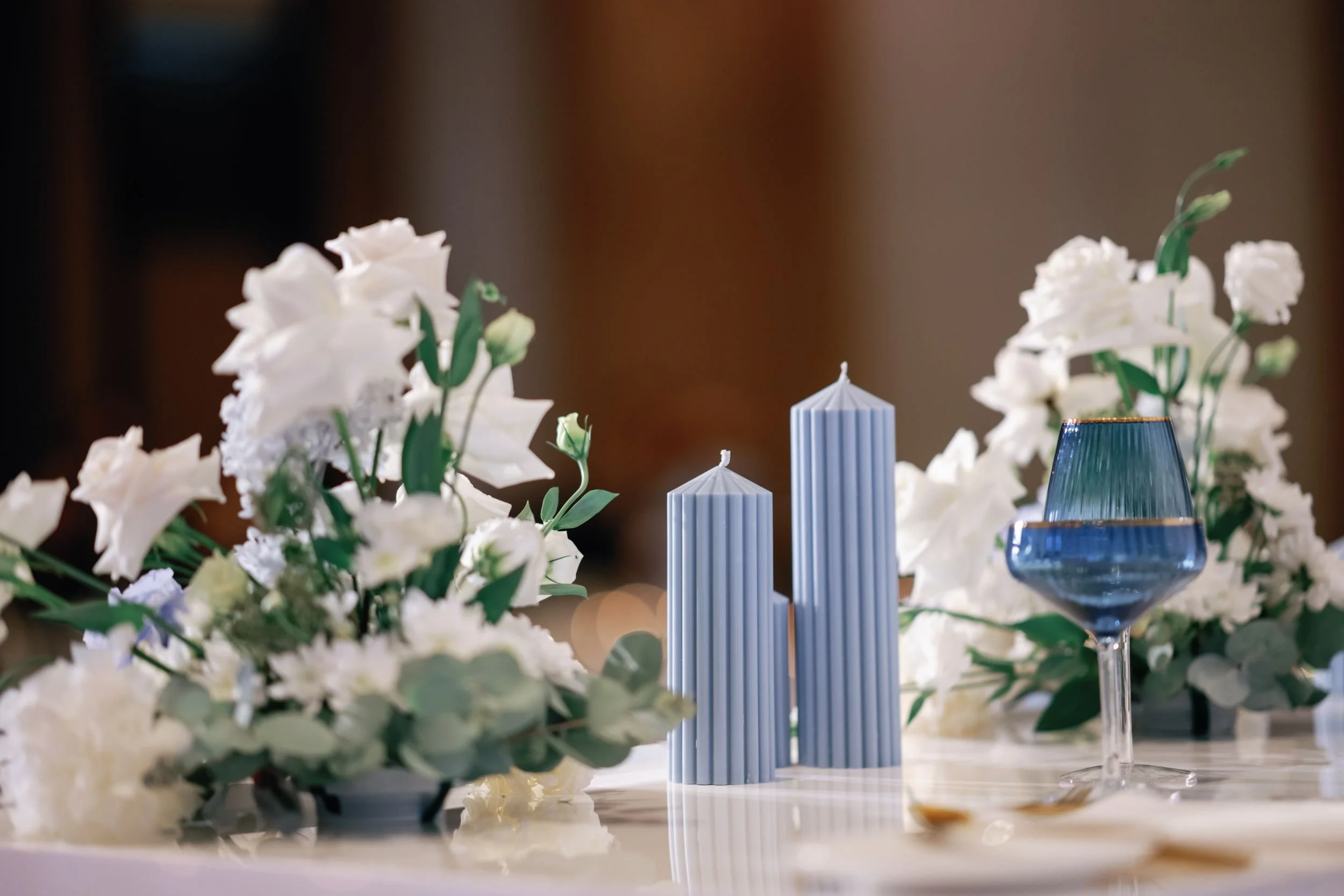 Photo by Norman Yapp Photography.  Close-up of white flowers and candles on a table, with blurred background.