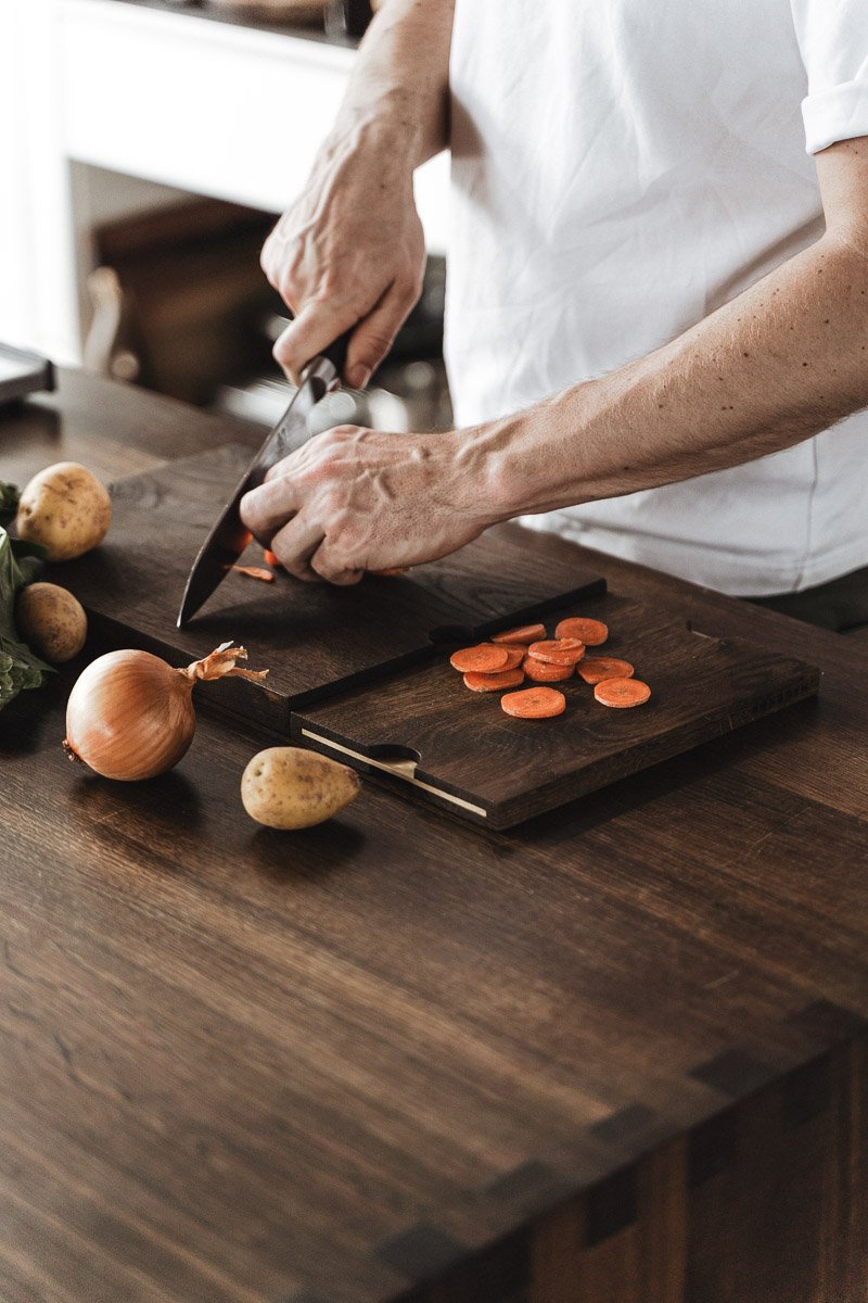 HC01 cutting board made of smoked oak with brass details, shown in use for food preparation