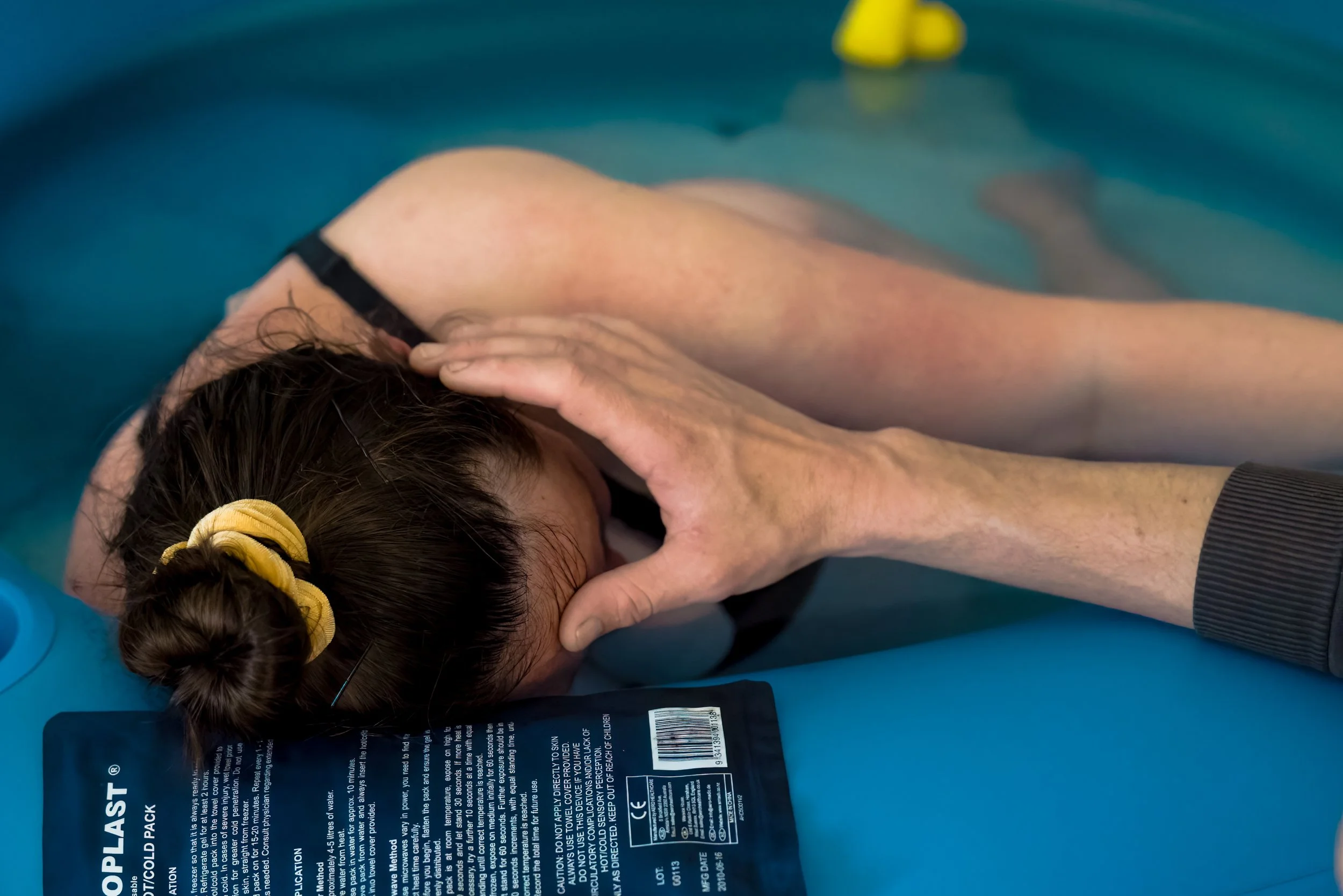 Person receiving support while leaning against a pool edge during labor in water.