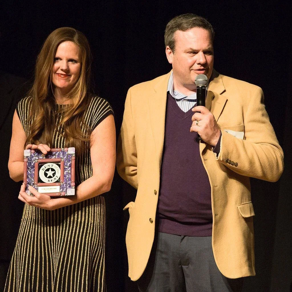 A woman holding a small picture frame and a man speaking into a microphone.