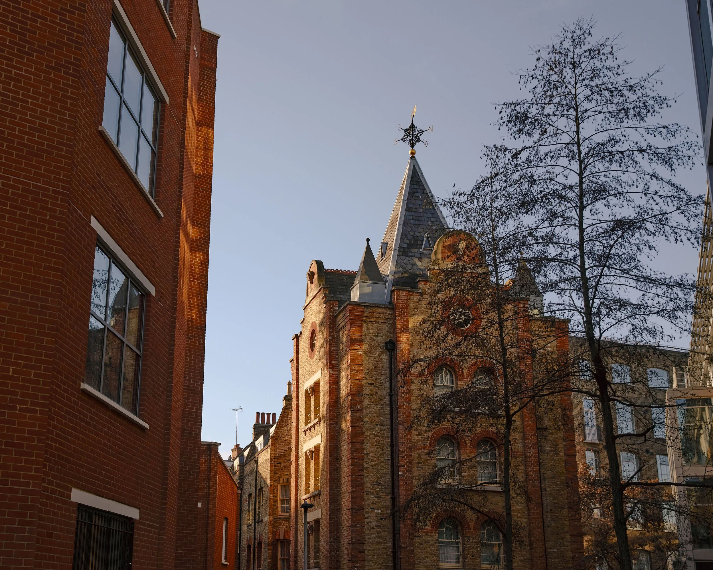 An ornate older building catching warm evening light among modern buildings in London.
