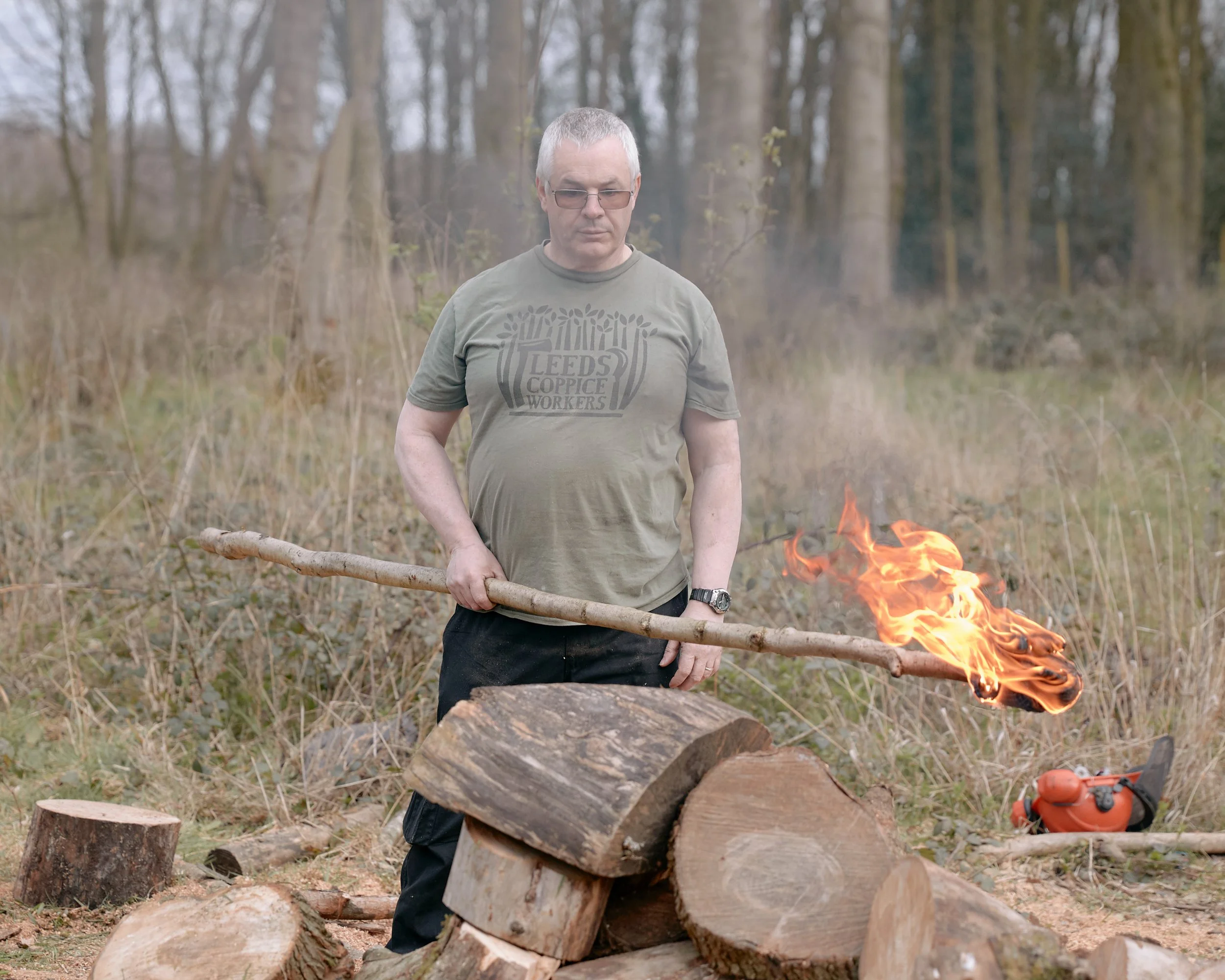 A man holding a burning torch to ignite a charcoal kiln in Yorkshire, England.