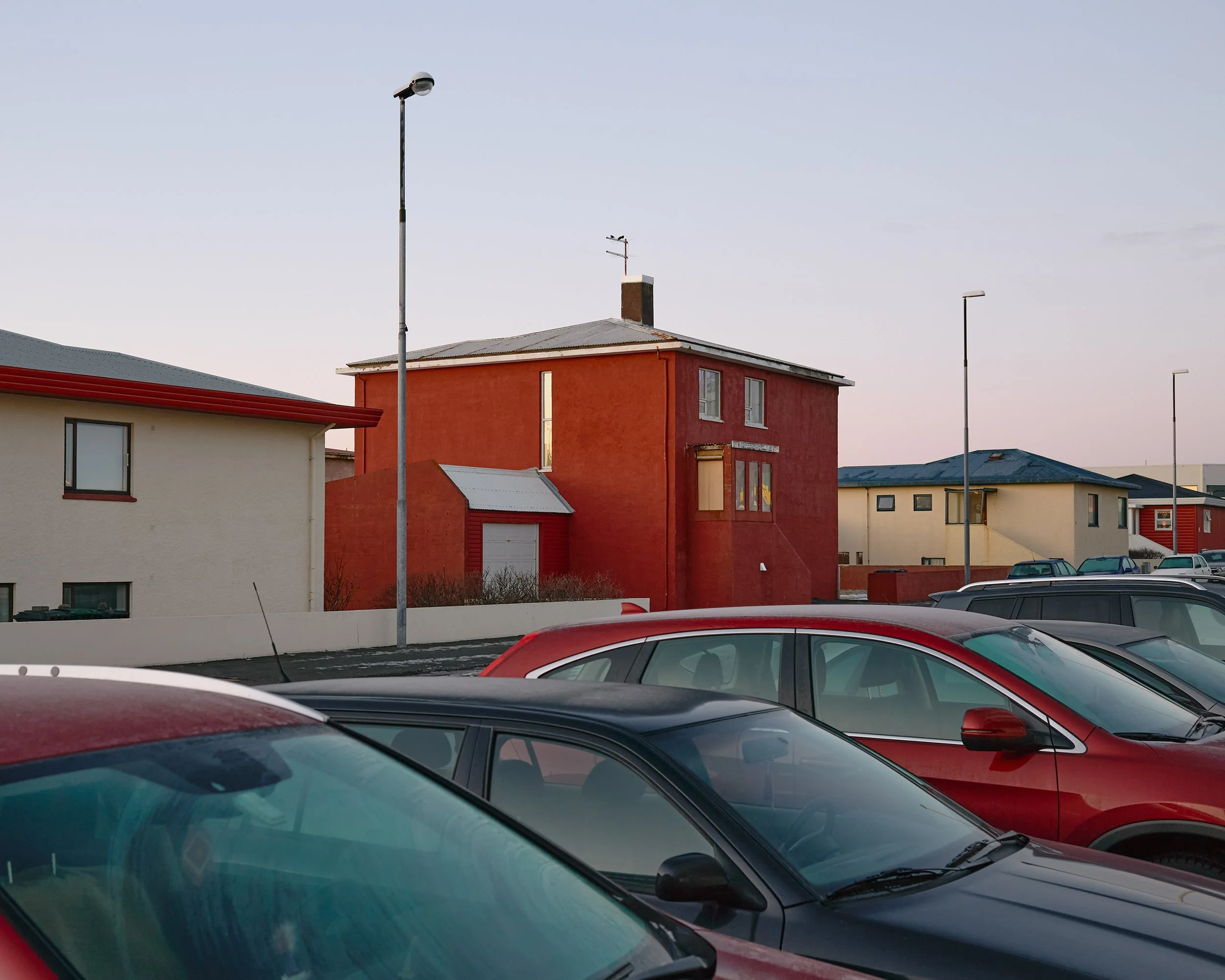 Parked cars reflecting pale morning light in front of detached homes in Keflavík.