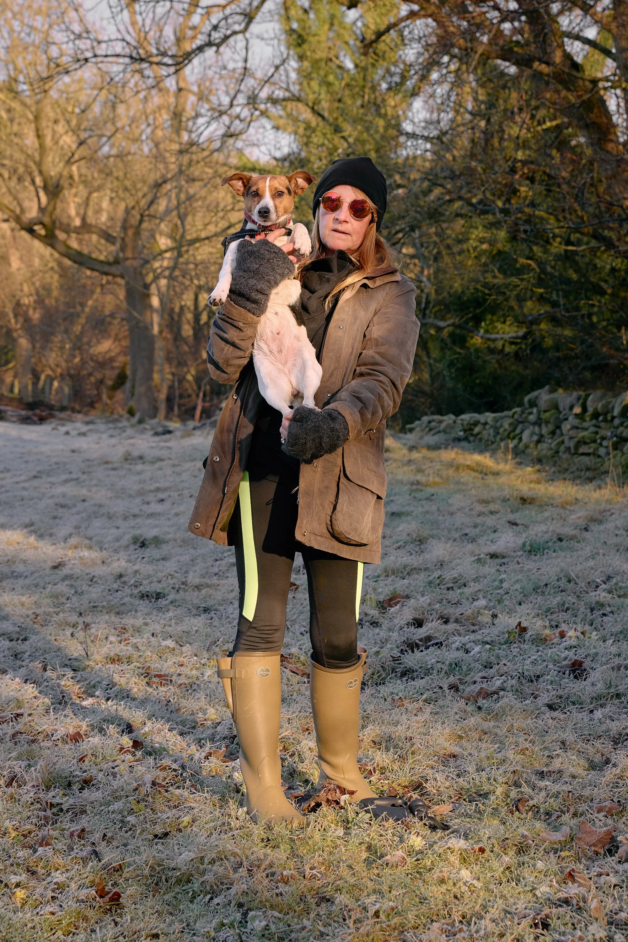 A woman holding a Jack Russell dog in warm, low sunlight in Yorkshire, England.