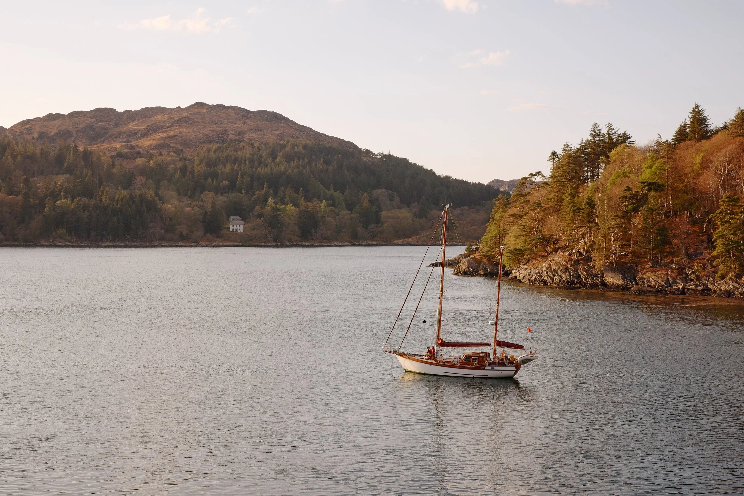 A sailing yacht anchored near a small wooded island on Loch Moidart.