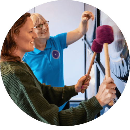 The tutor Helen with a student in front of a Paiste 38" Symphonic gong. The student has a gong mallet in each hand. Both women are smiling.