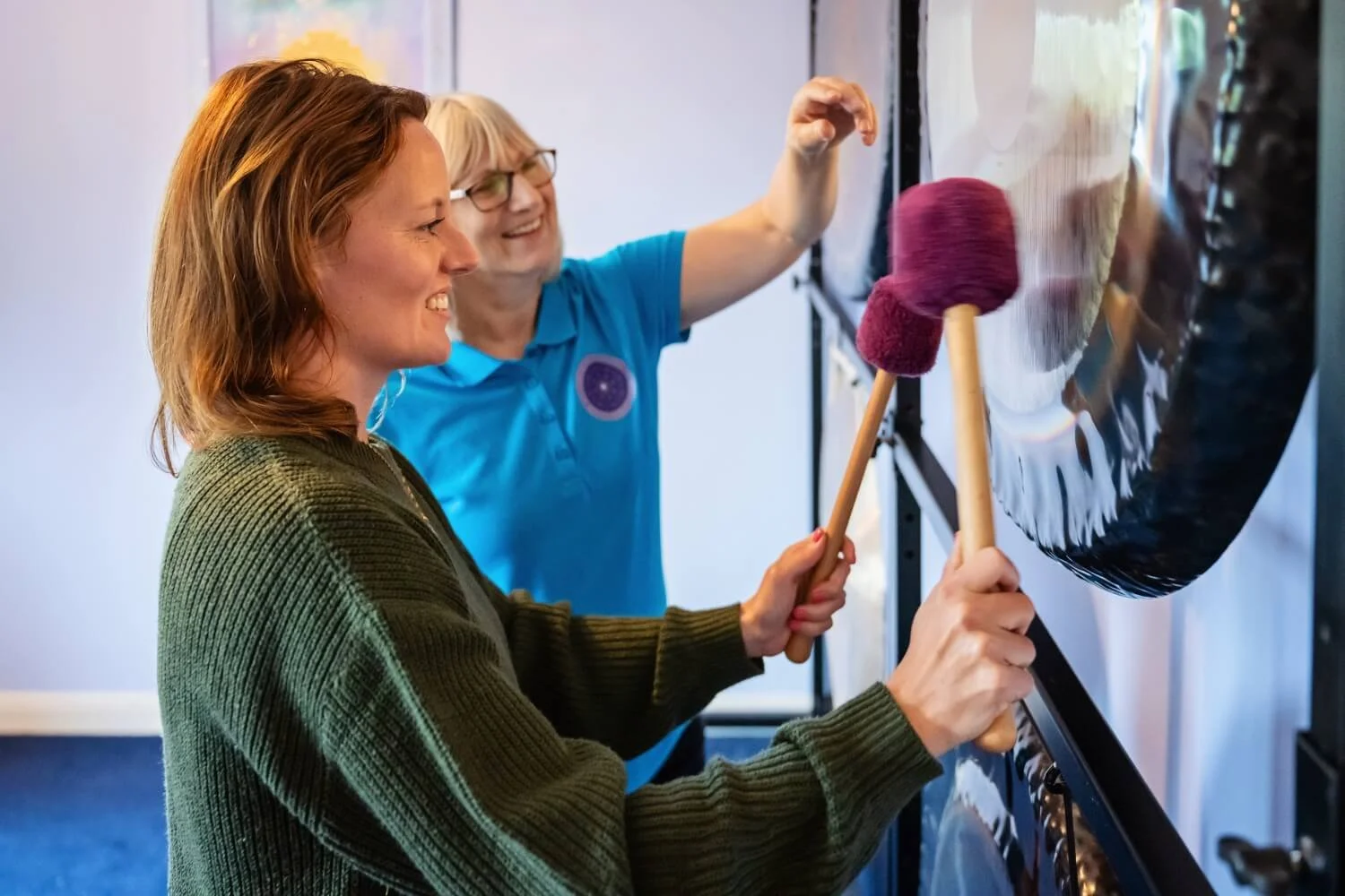 Hands-on sound healing training mentorship session at the Academy of Sound Therapy, showing the tutor Helen Campbell guiding a practitioner student on proper gong playing techniques during the practitioner diploma course near Grantham.