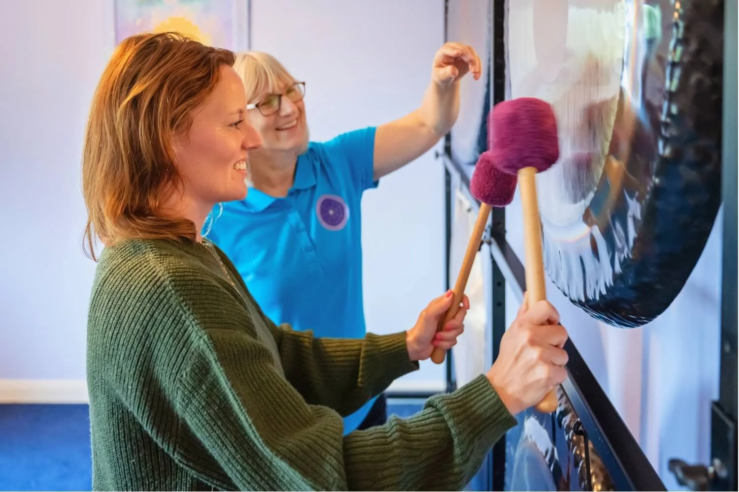 A professional gong mastery training session at the Academy of Sound Therapy near Grantham, showing the tutor Helen Campbell giving practical, hands-on instruction to a practitioner student on advanced mallet stroke techniques.