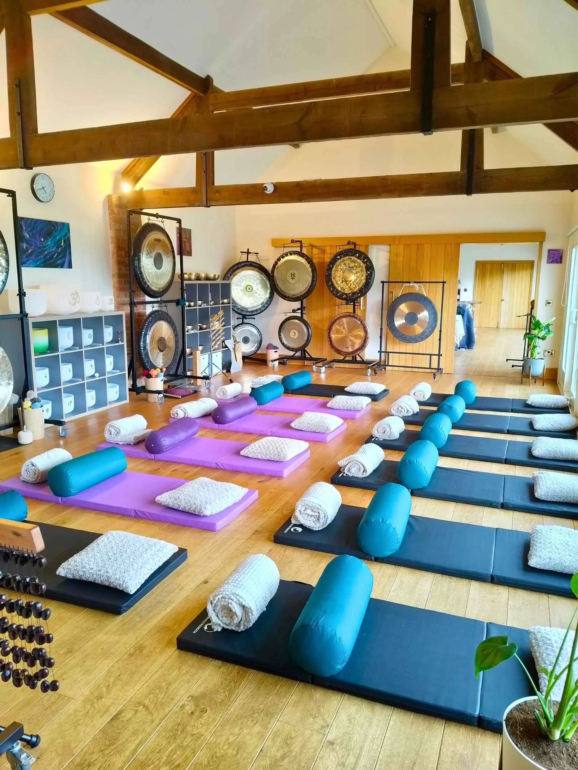 The main teaching room at the academy set out ready for a sound bath. There are 12 comfy mats laid out on the floor, each with a pillow, bolster and blanket. Along the back wall are gongs, crystal and Himalayan sing bowls and percussion instruments.