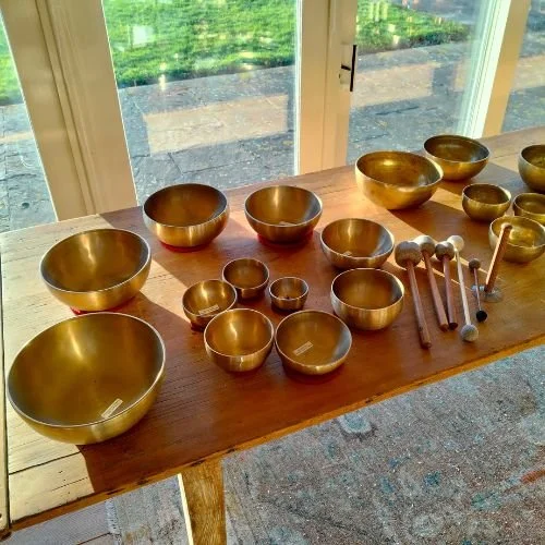 A  large selection of Himalayan singing bowls laid out on top of a long wooden table in a fibonacci spiral  - bringing in sacred geometry!