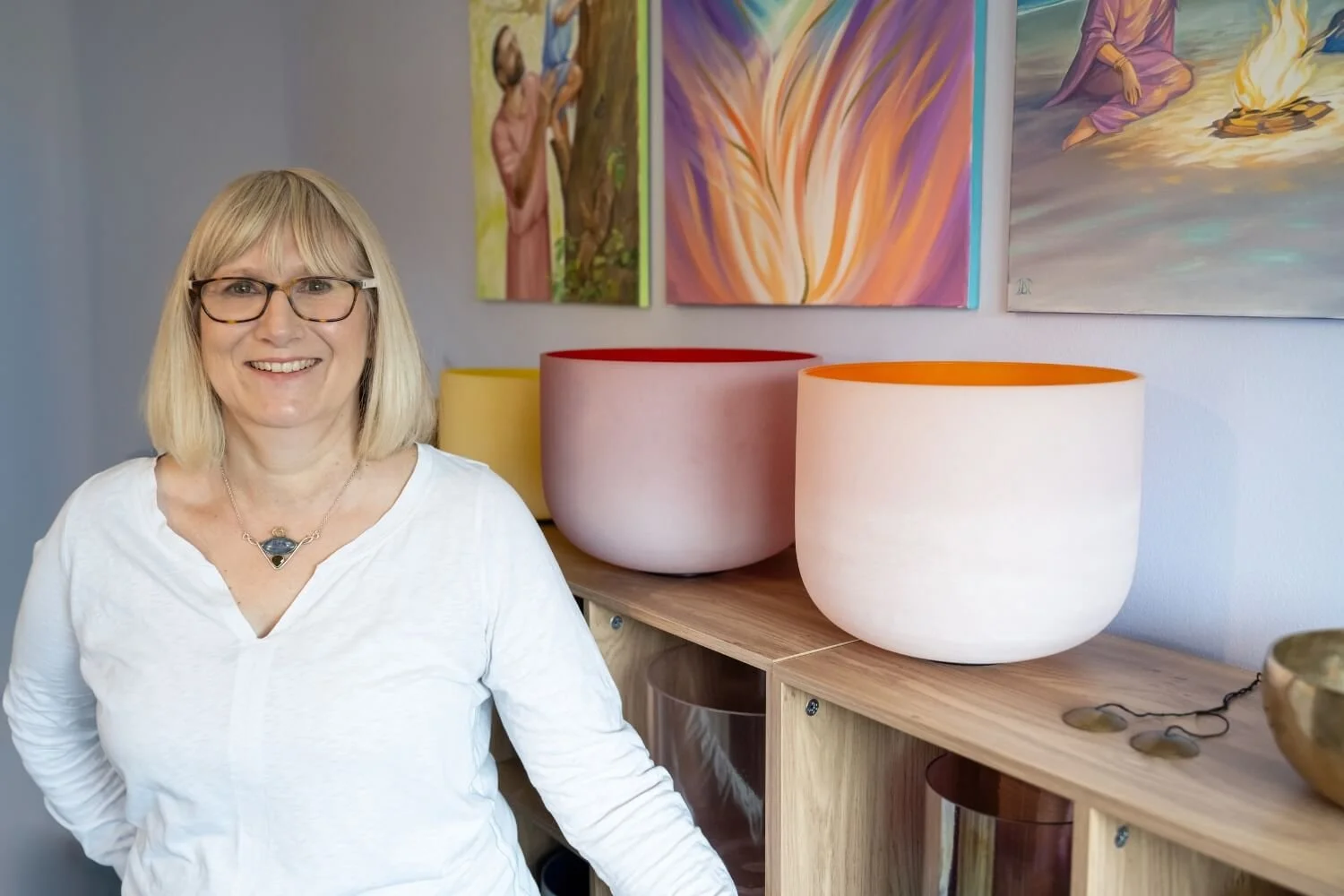 Professional sound therapy teacher and academy founder Helen Campbell standing mindfully beside a collection of frosted crystal singing bowls inside her quiet countryside training studio near Grantham.
