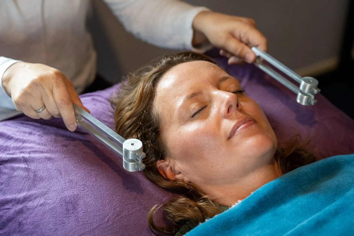 Sound therapy teacher Helen Campbell demonstrating the precise application of weighted OM tuning forks near a client's ears to restore nervous system balance during an accredited training day near Grantham.