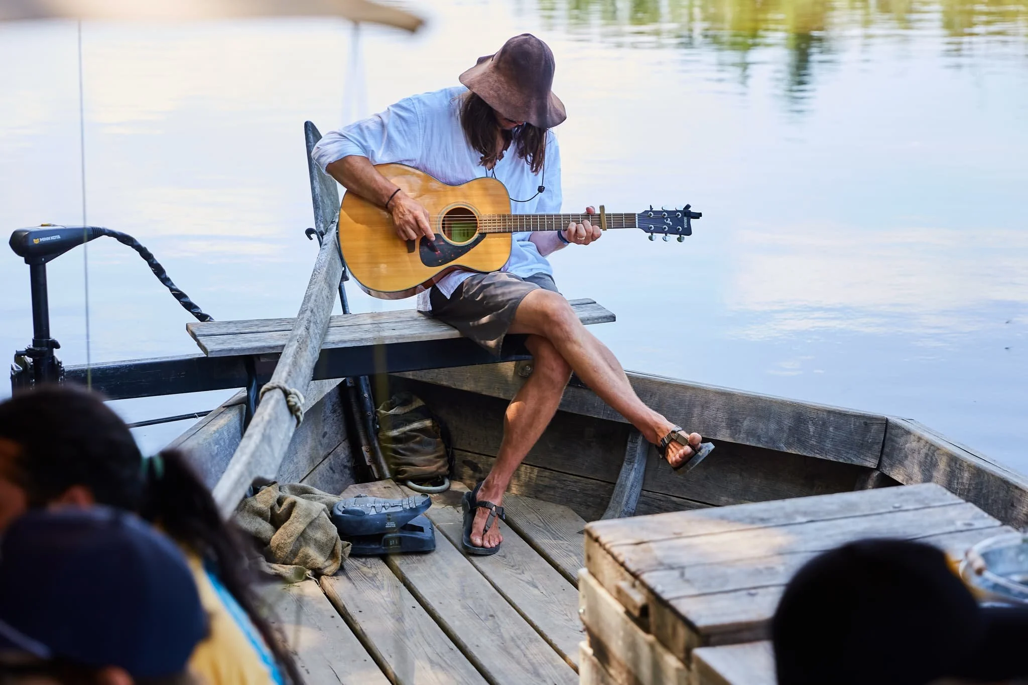 A man in a large hat playing an acoustic guitar on a wooden boat.