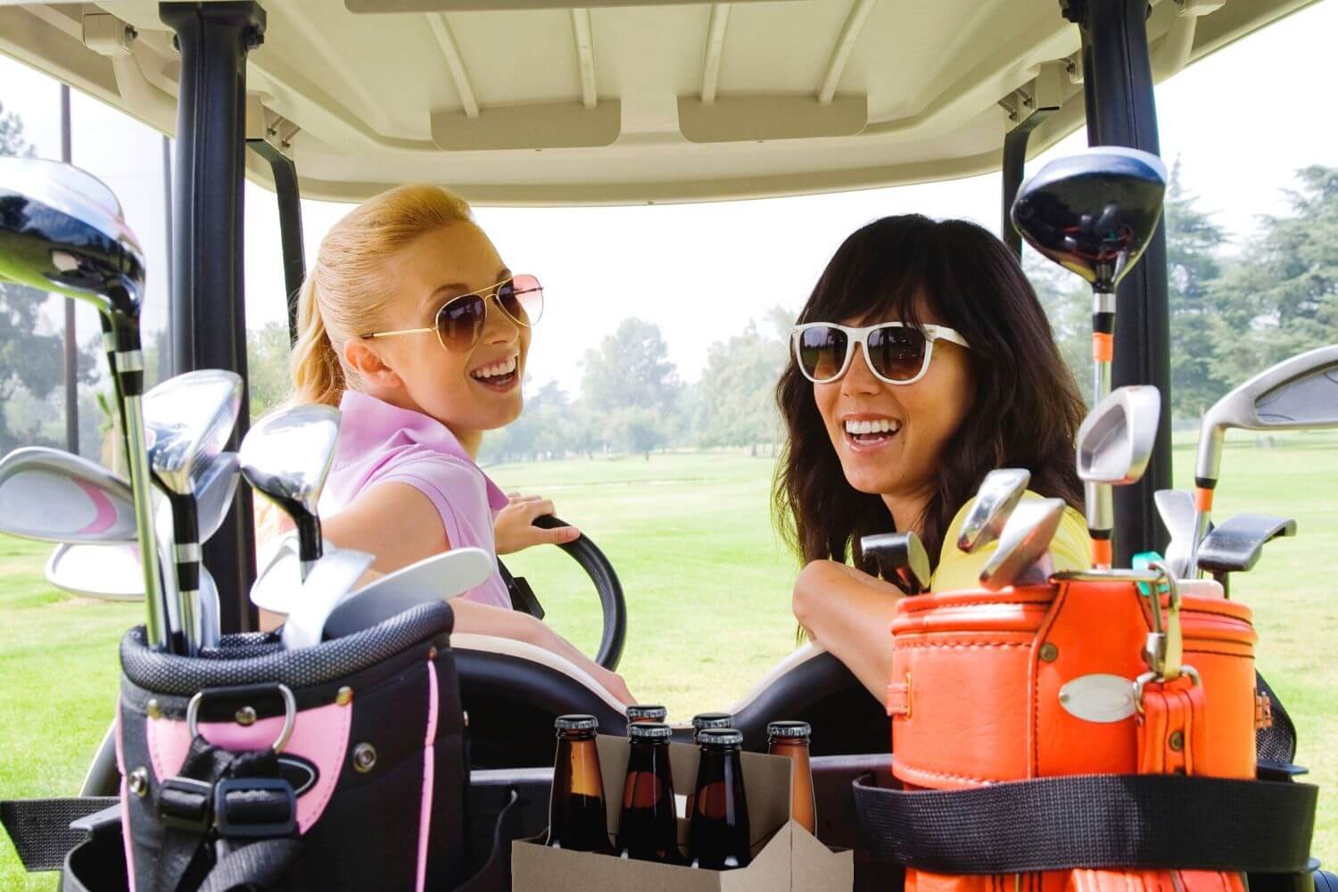 two happy women in a golf cart with equipment and beer