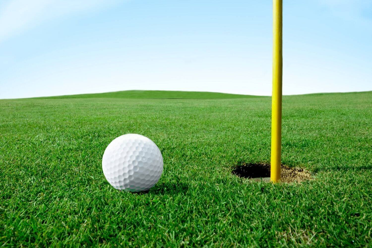 Golf ball next to hole with flagpole