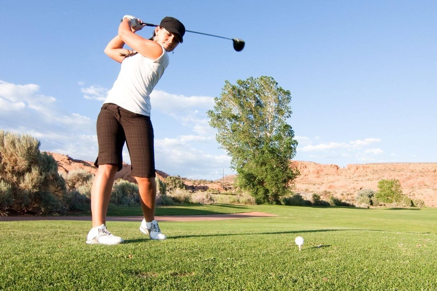 Woman swinging a driver to hit the golf ball off of the tee