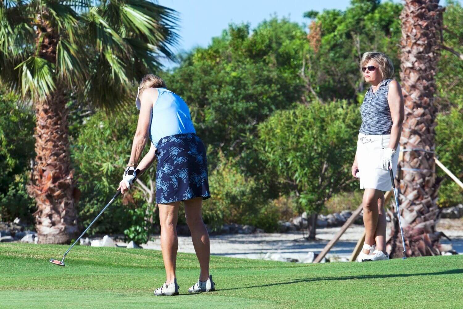Older woman golfer swinging club while another woman golfer watches and waits for her turn