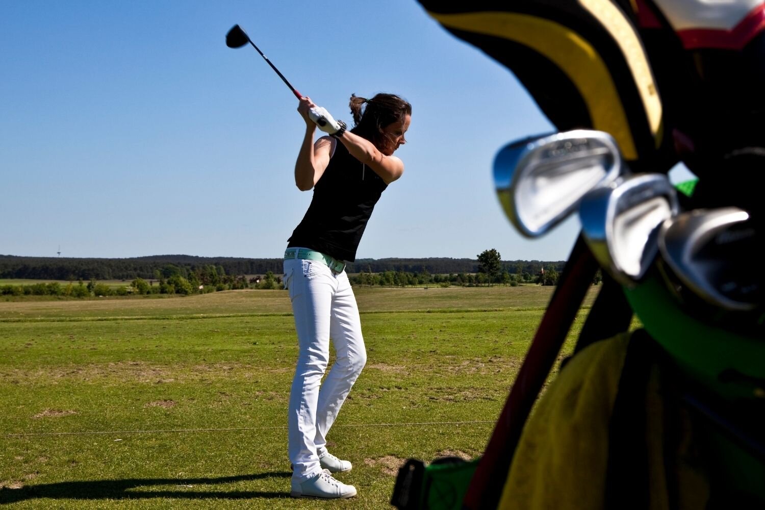 Female golfer hitting golf ball with bag of clubs nearby