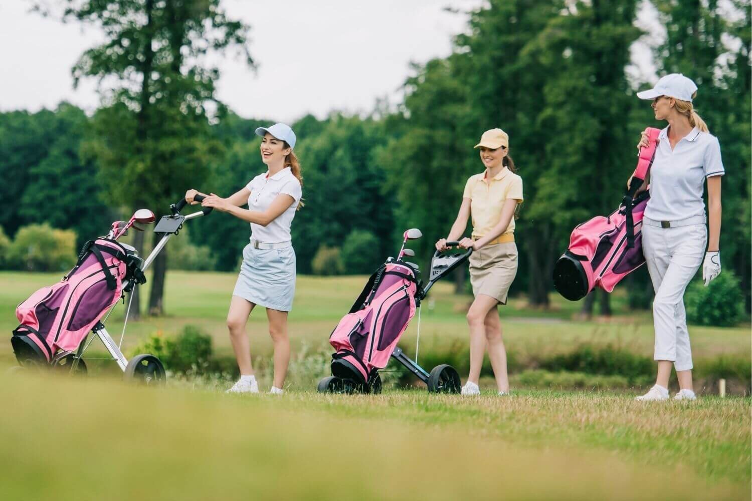 Three women golfers wearing different outfits carrying golf equipment