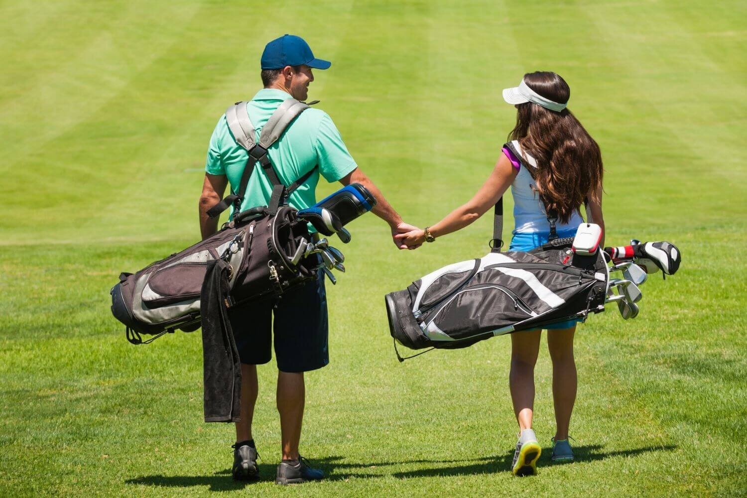 Male and female golfer holding hands on the golf course while carrying golf club bags