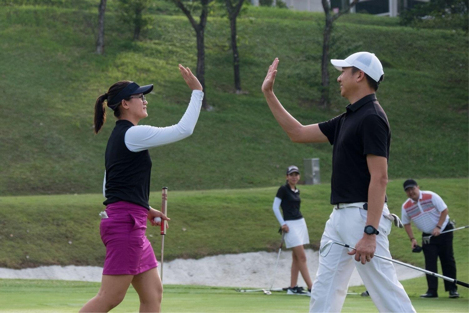 Female and male golfers giving each other a high five on the course