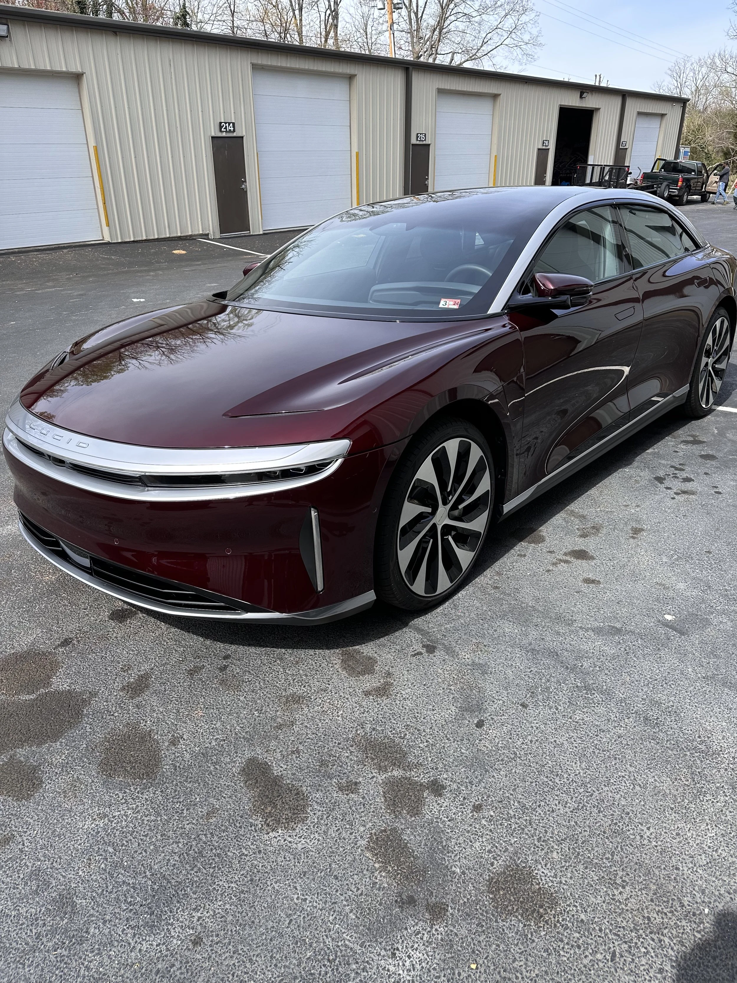 A sleek maroon electric car parked in front of a storage unit facility with four garage doors.