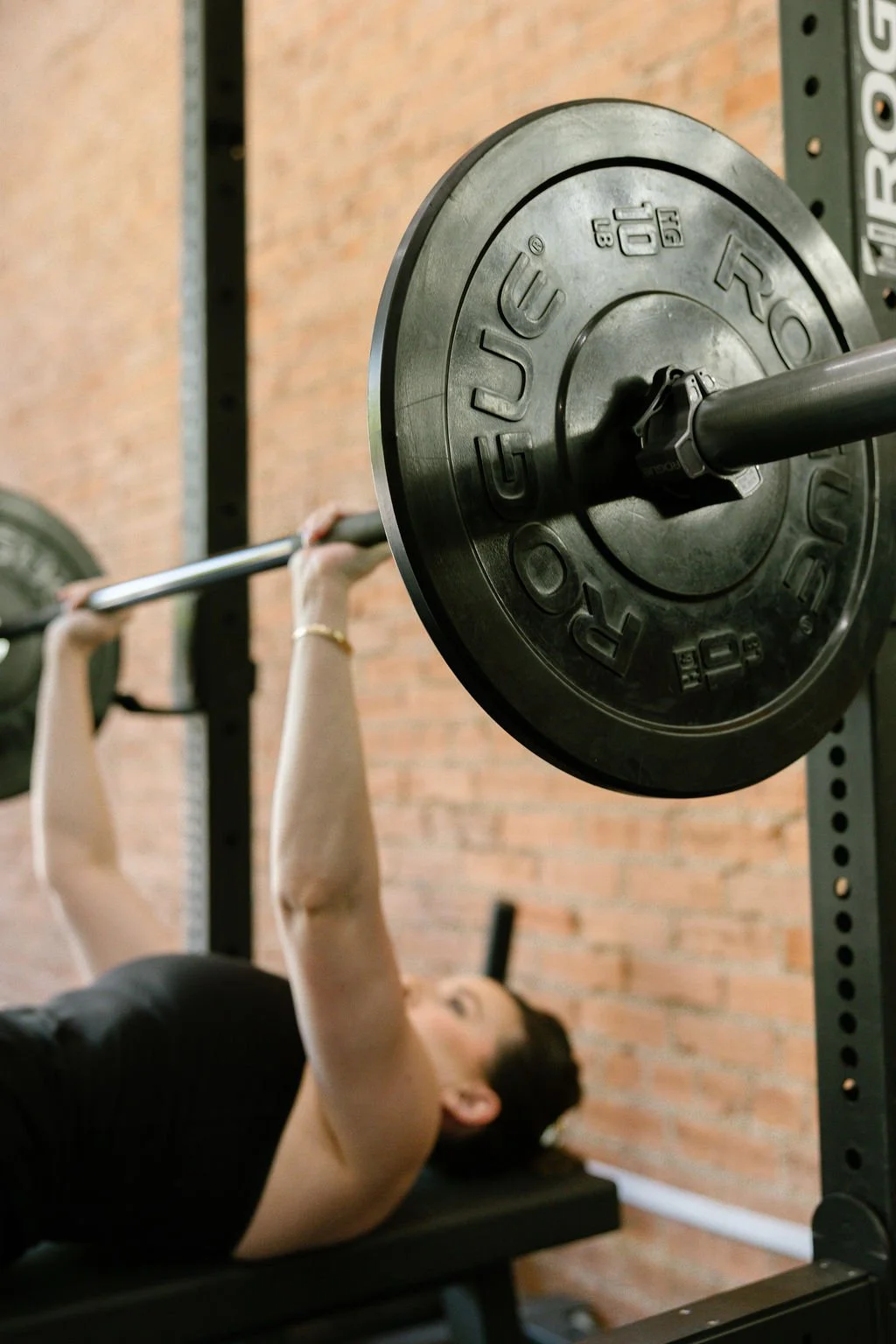Elena Lee's in-person training client bench presses weights at her studio in Dallas, Tx.