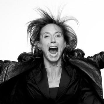 A black and white head and shoulders  shot of Andrea Sullivan. Looks like she is jumping in the air with excitement