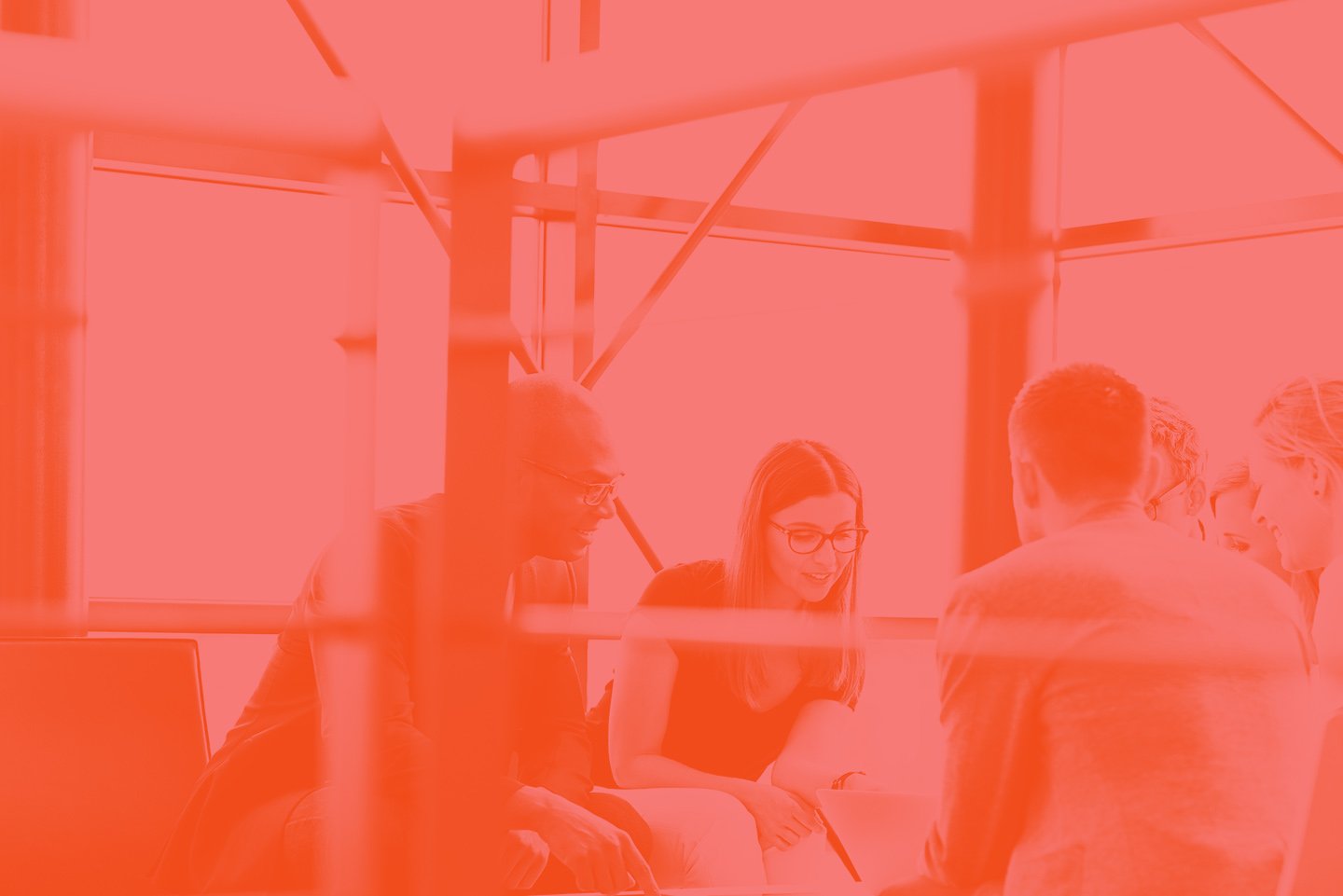 Group of five people sitting around a table in a meeting room, engaging in conversation.