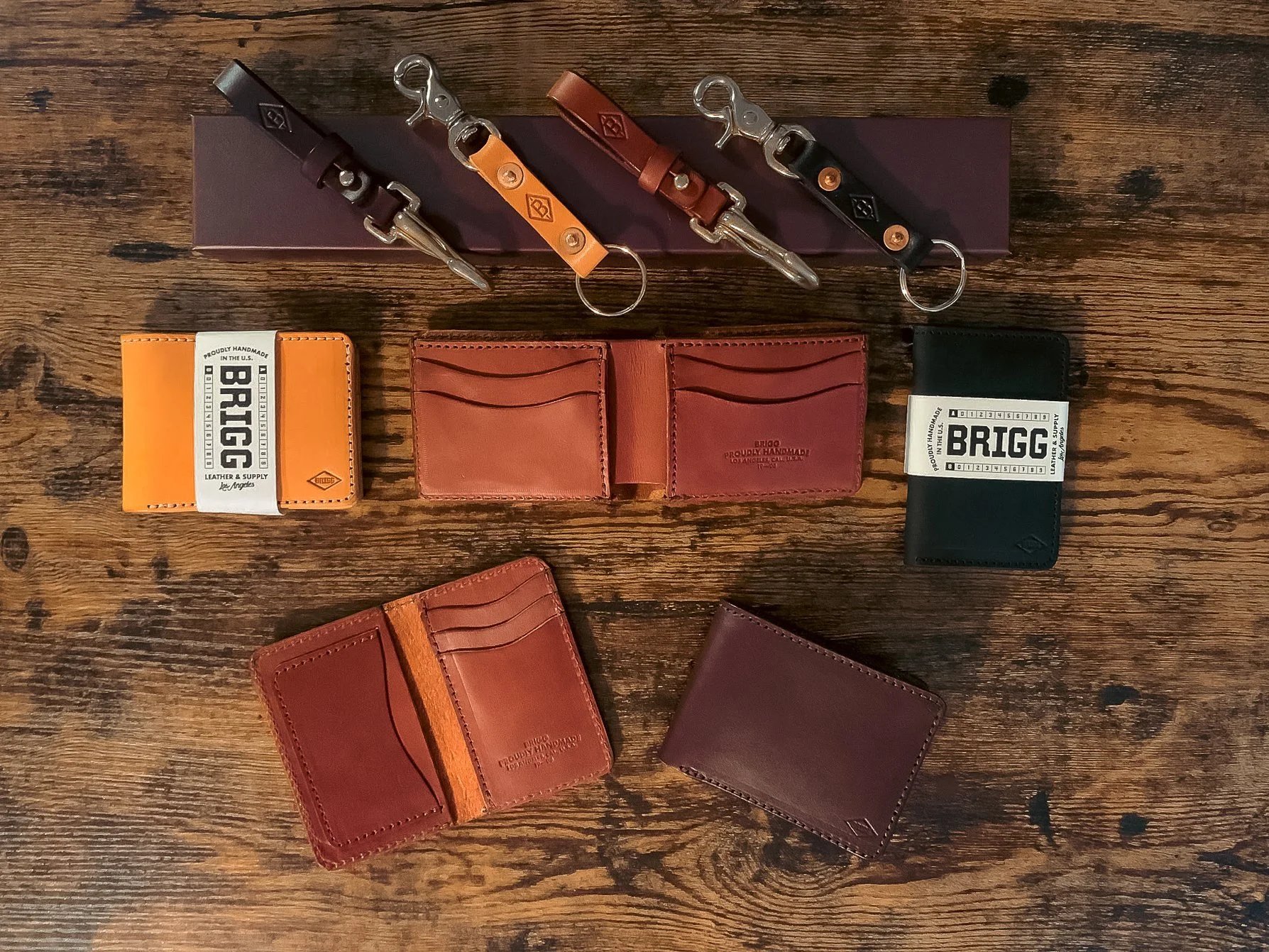 Collection of leather wallets, keychains, and cardholders arranged on a wooden surface.