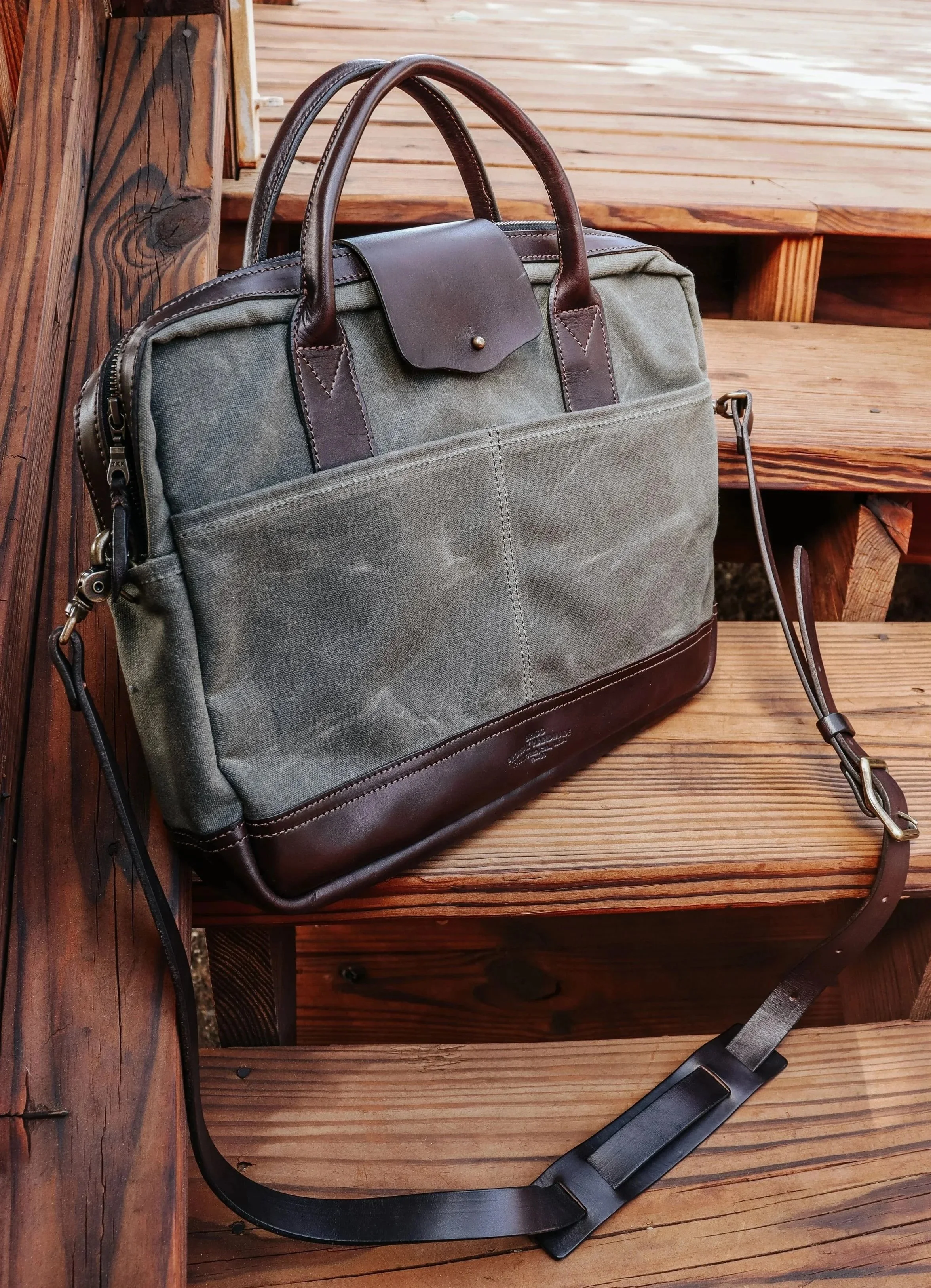 A leather shoulder strap resting on a wooden surface with a briefcase partially visible.