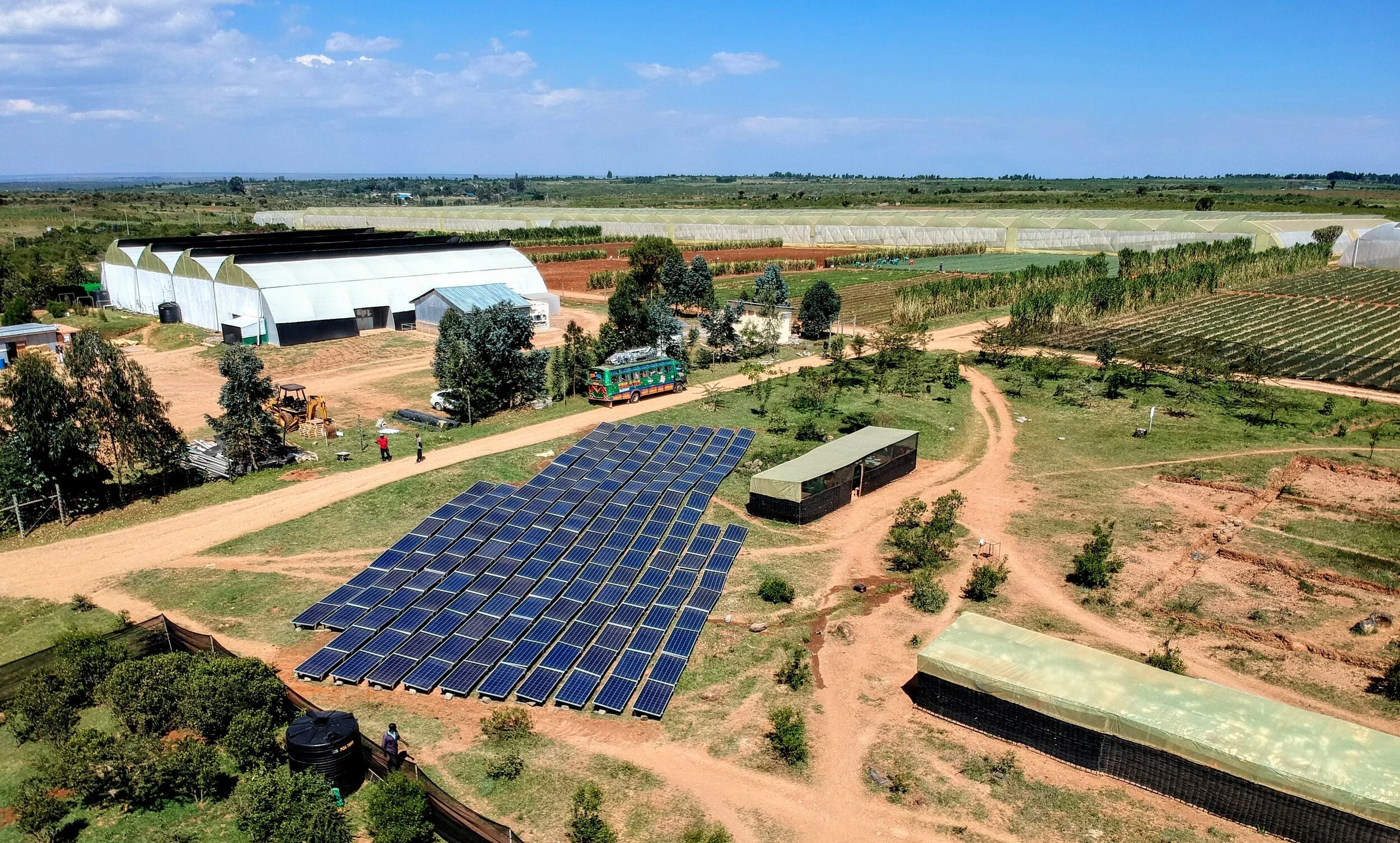 An image of solar panels on a farm. The solar panels are surrounded by roads and crop fields in the back with farmers looking at the panels.
